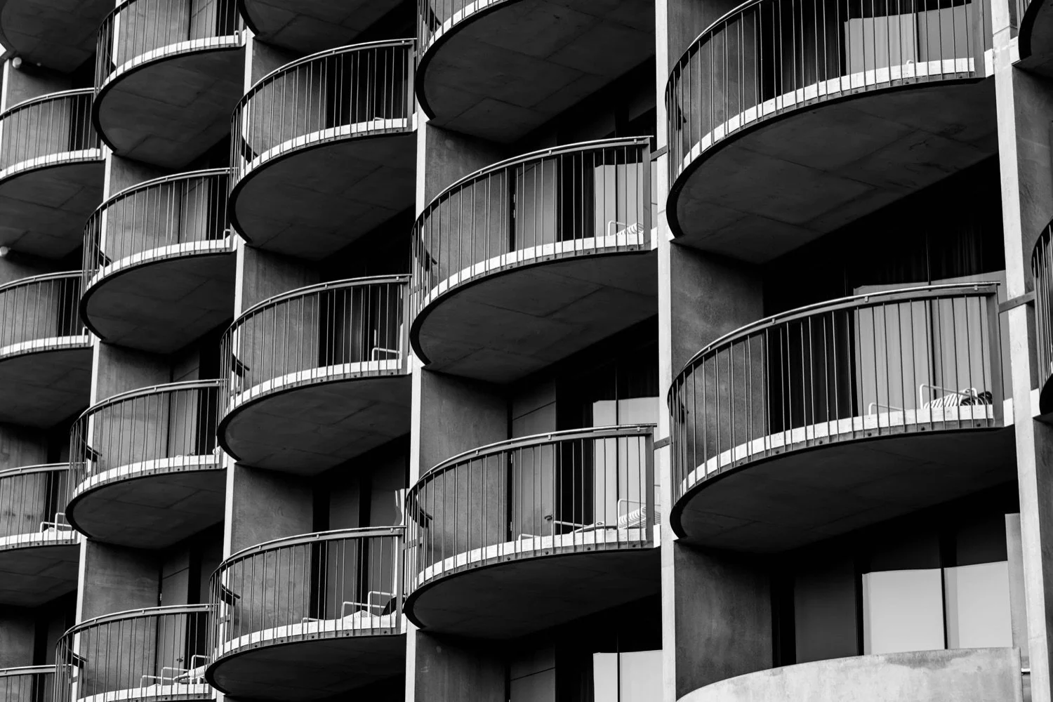 Black and white photo of a multi-story building with curved balconies on each floor, featuring railing designs and a chair on some balconies.