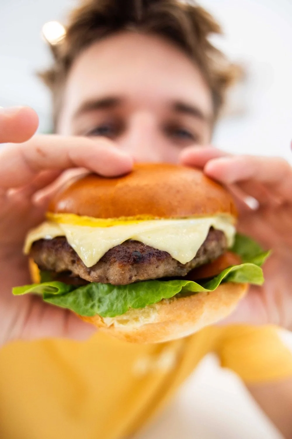 Person holding a cheeseburger with lettuce, cheese, beef patty, and bun.