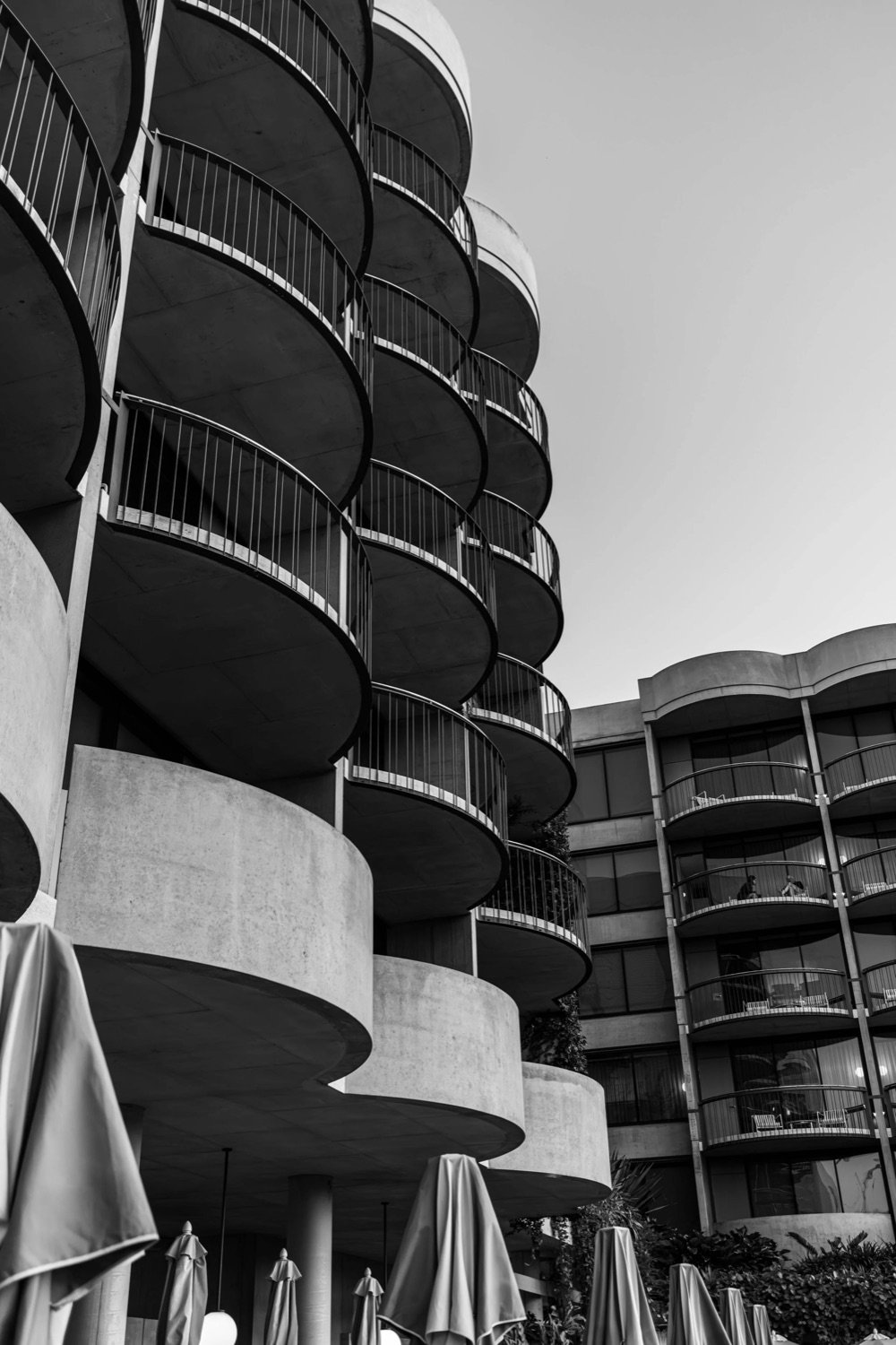 Black and white photo of modern residential building with curved balconies and glass railings, seen from below against a cloudy sky.
