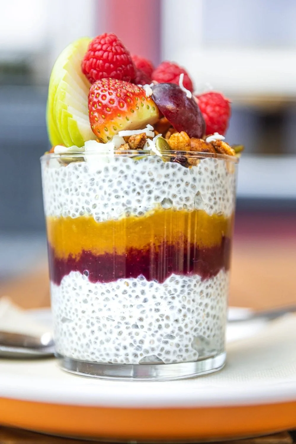 Layered chia pudding with topped fresh strawberries, raspberries, sliced apple, grapes, and granola in a glass
