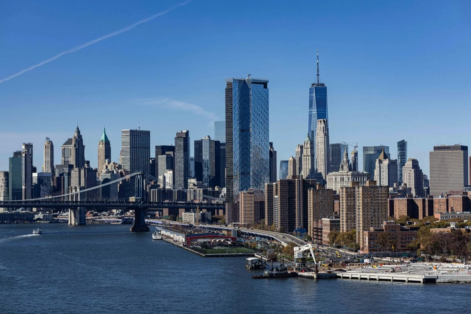 Skyscrapers and buildings of Manhattan skyline with a bridge crossing a river in New York City on a clear day.