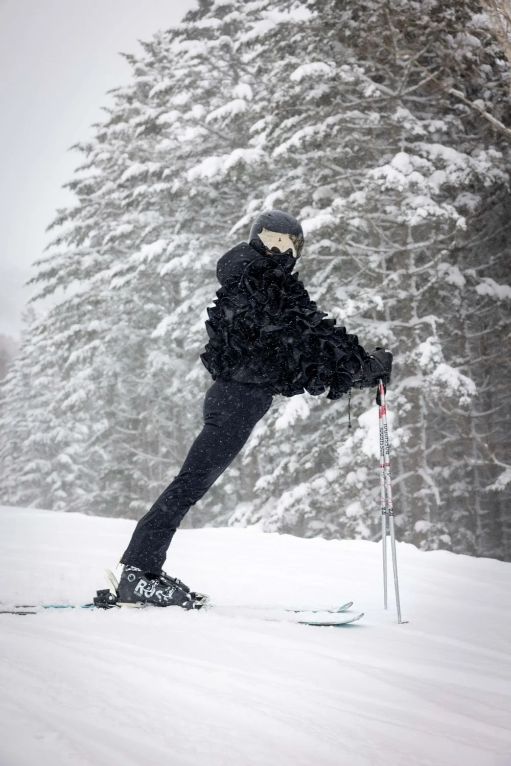 Person dressed in black skiing in snowy forest with snow-covered trees in the background.