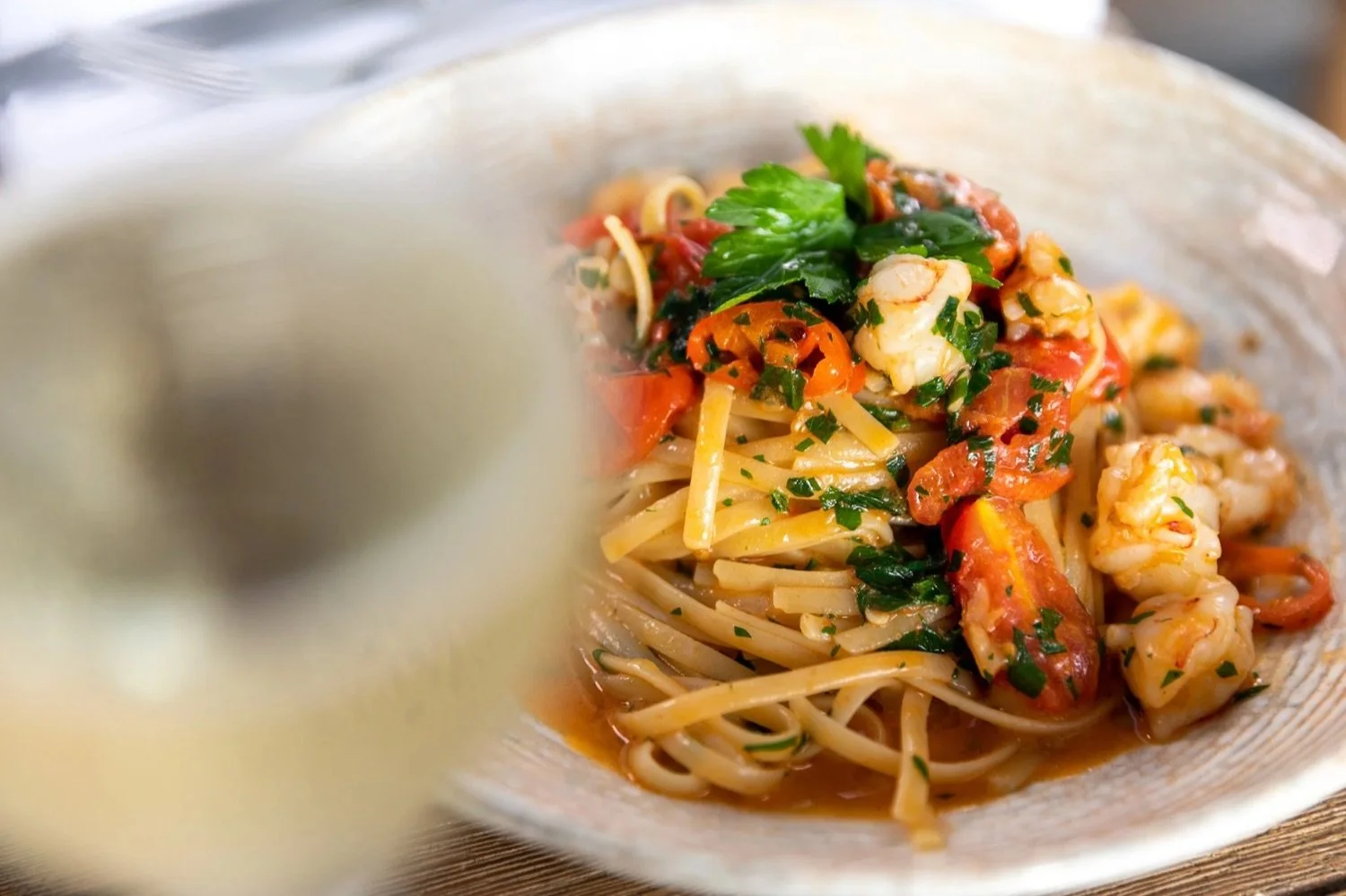 A bowl of pasta with shrimp, cherry tomatoes, herbs, and fresh basil.