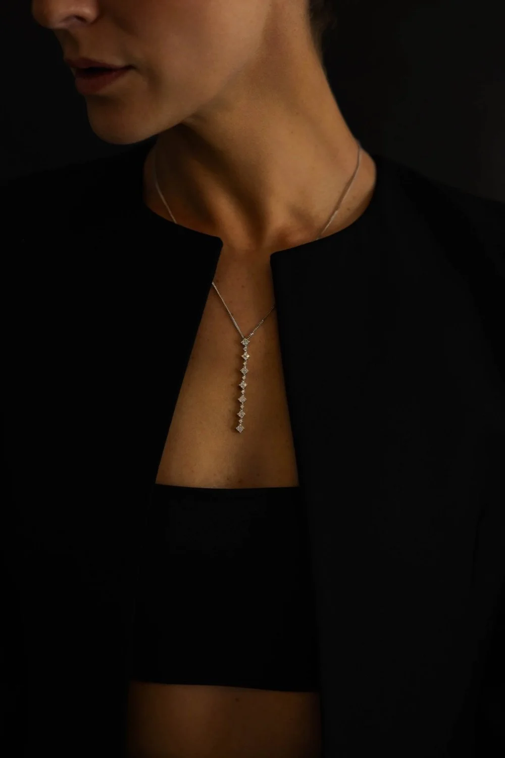 Close-up of a woman wearing a black top, a black jacket, and a silver necklace with a vertical row of diamonds.