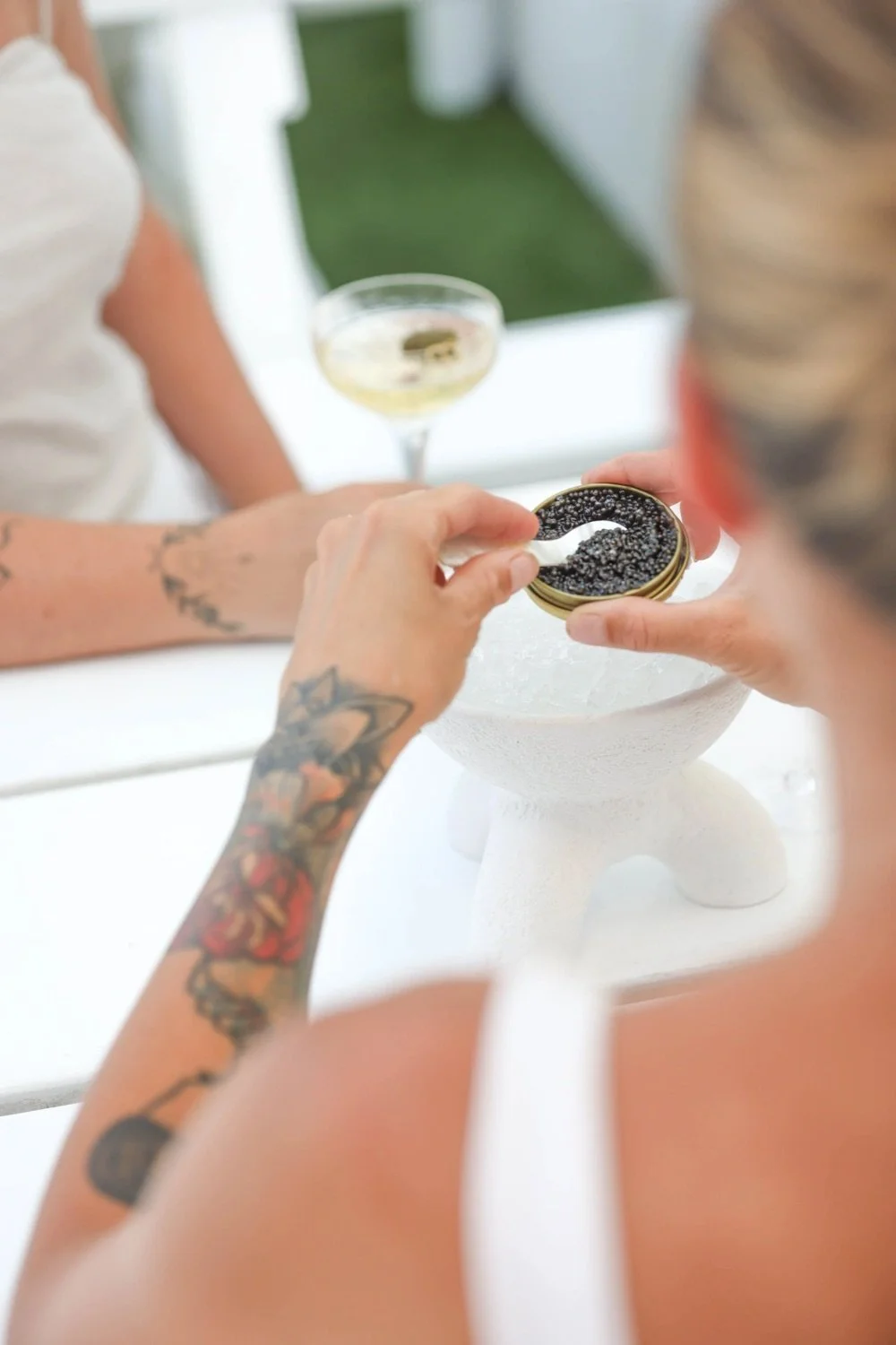 People are opening a tin of black caviar, with a cocktail glass of champagne in the background.