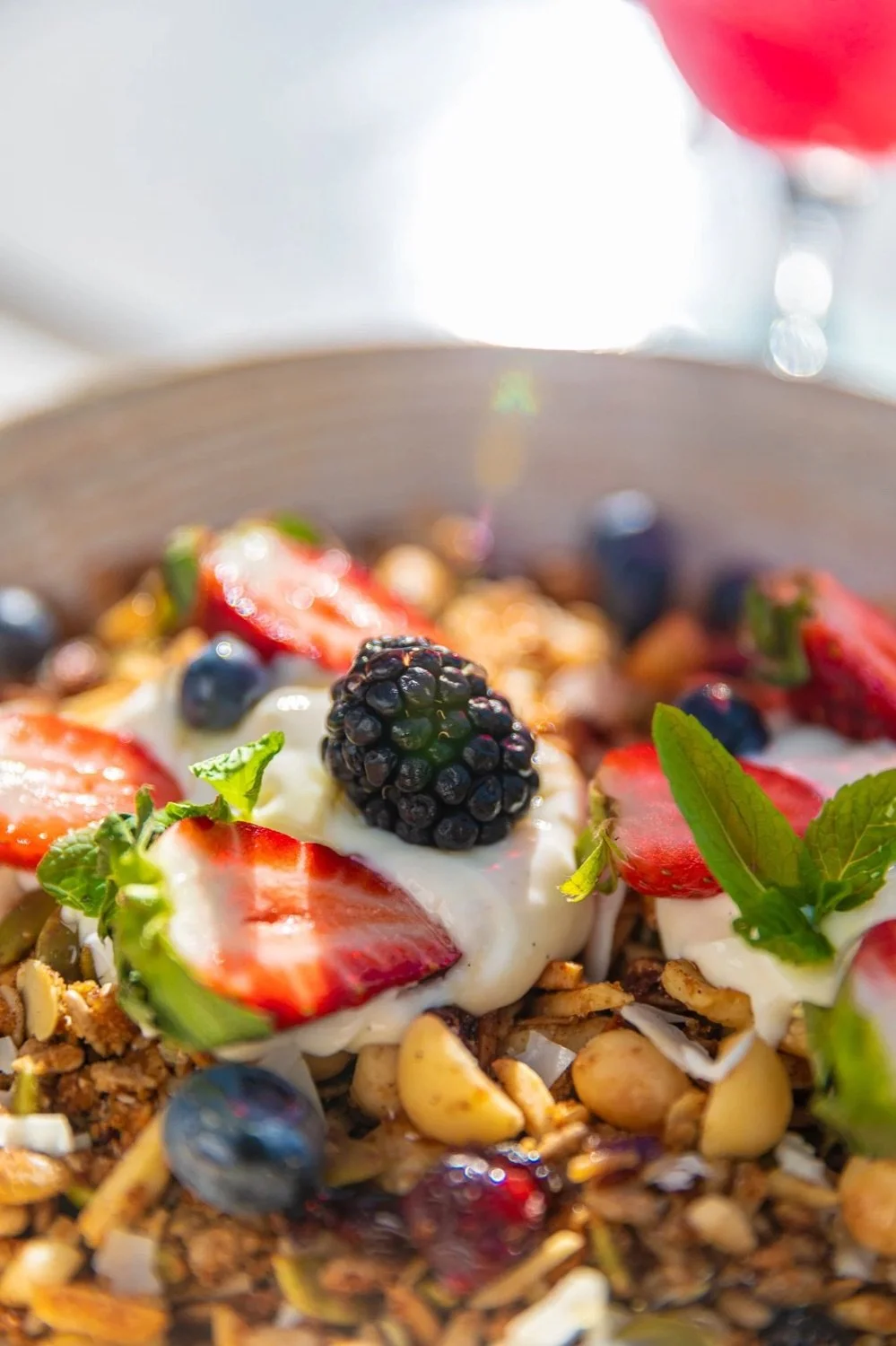 Close-up of a yogurt parfait topped with strawberries, blueberries, blackberries, granola, and fresh mint leaves.