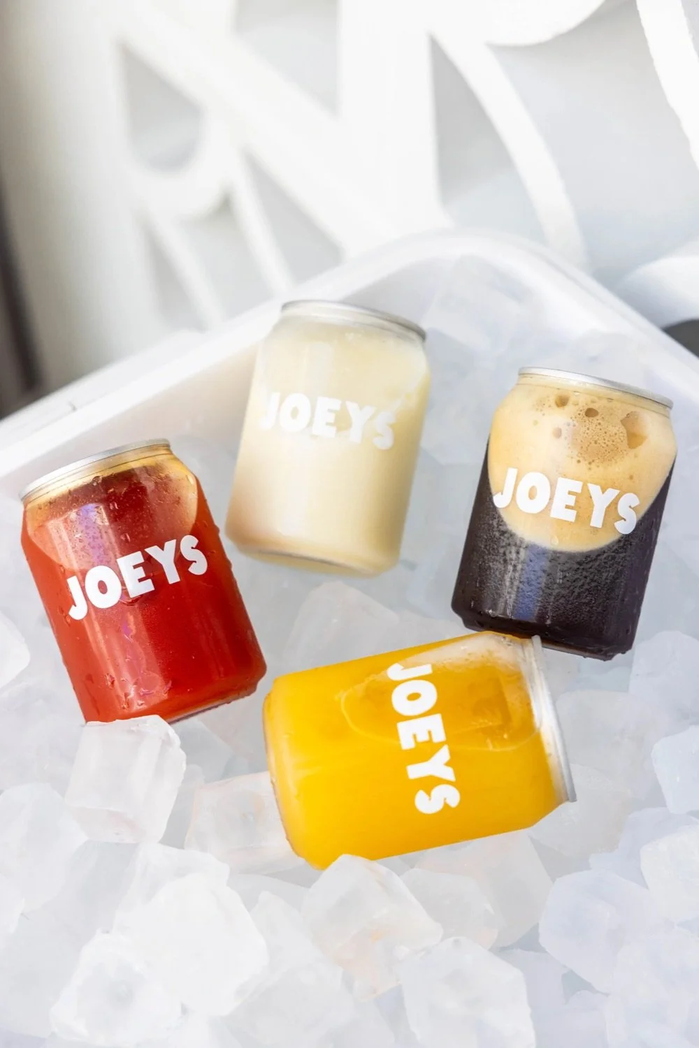 Four colorful canned beverages chilling on ice, with 'Joey's' printed on each can.