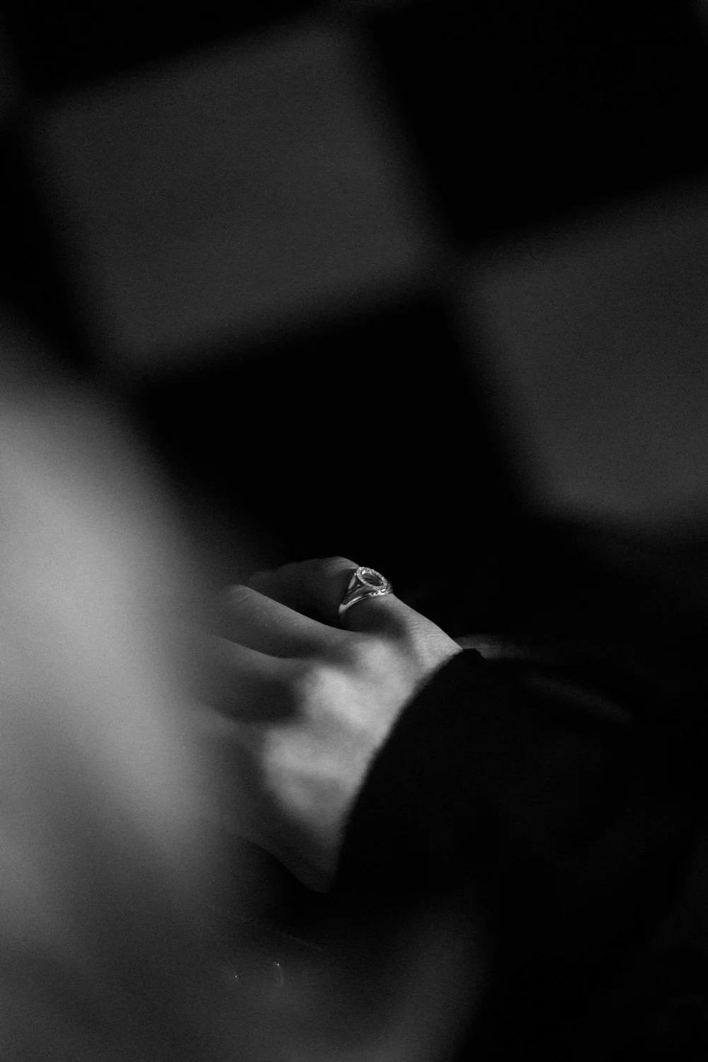 Close-up of a woman's hand wearing a ring, black and white photograph, blurred background.
