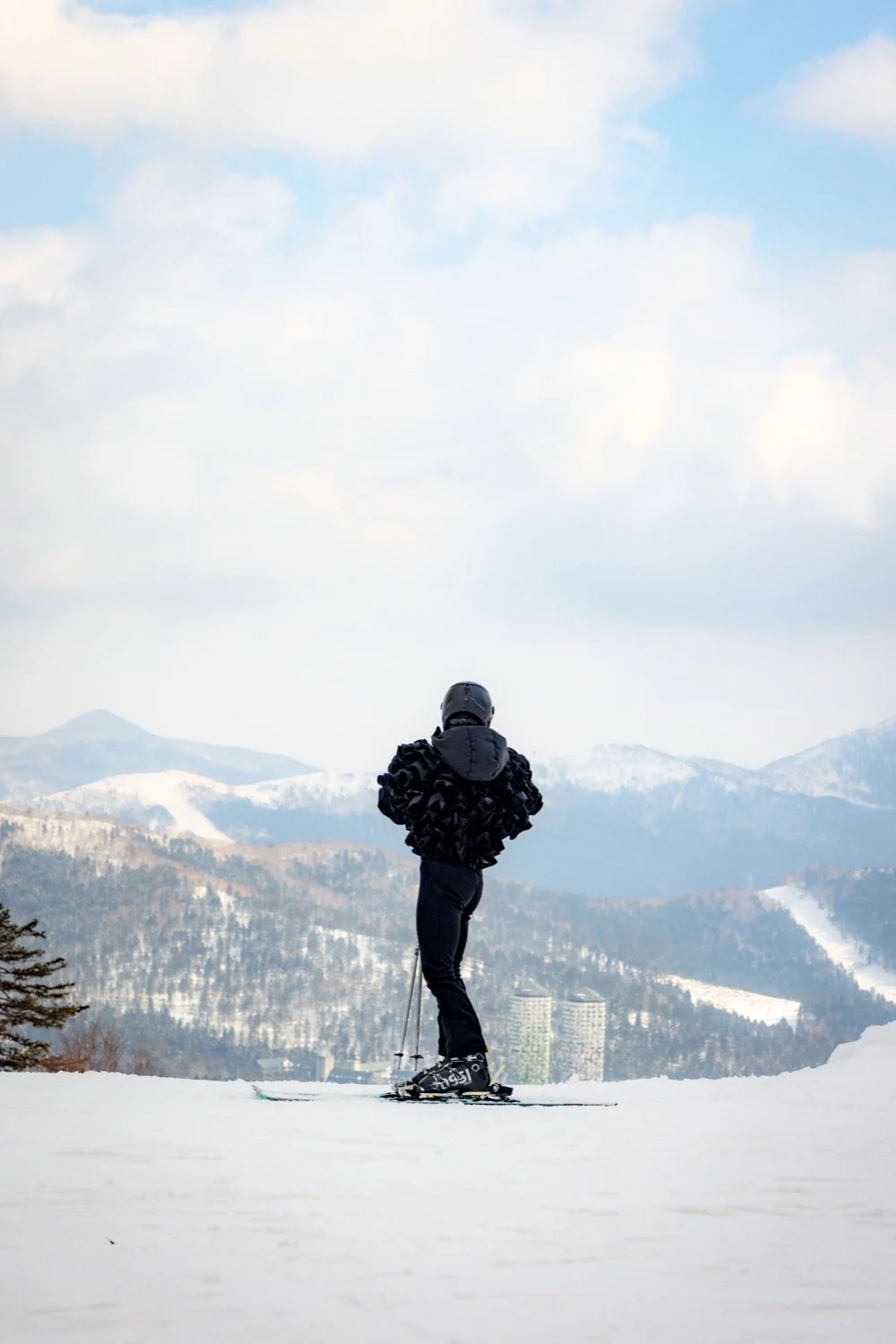 Person skiing on snow-covered slope with snow-capped mountains and cloudy sky in the background.