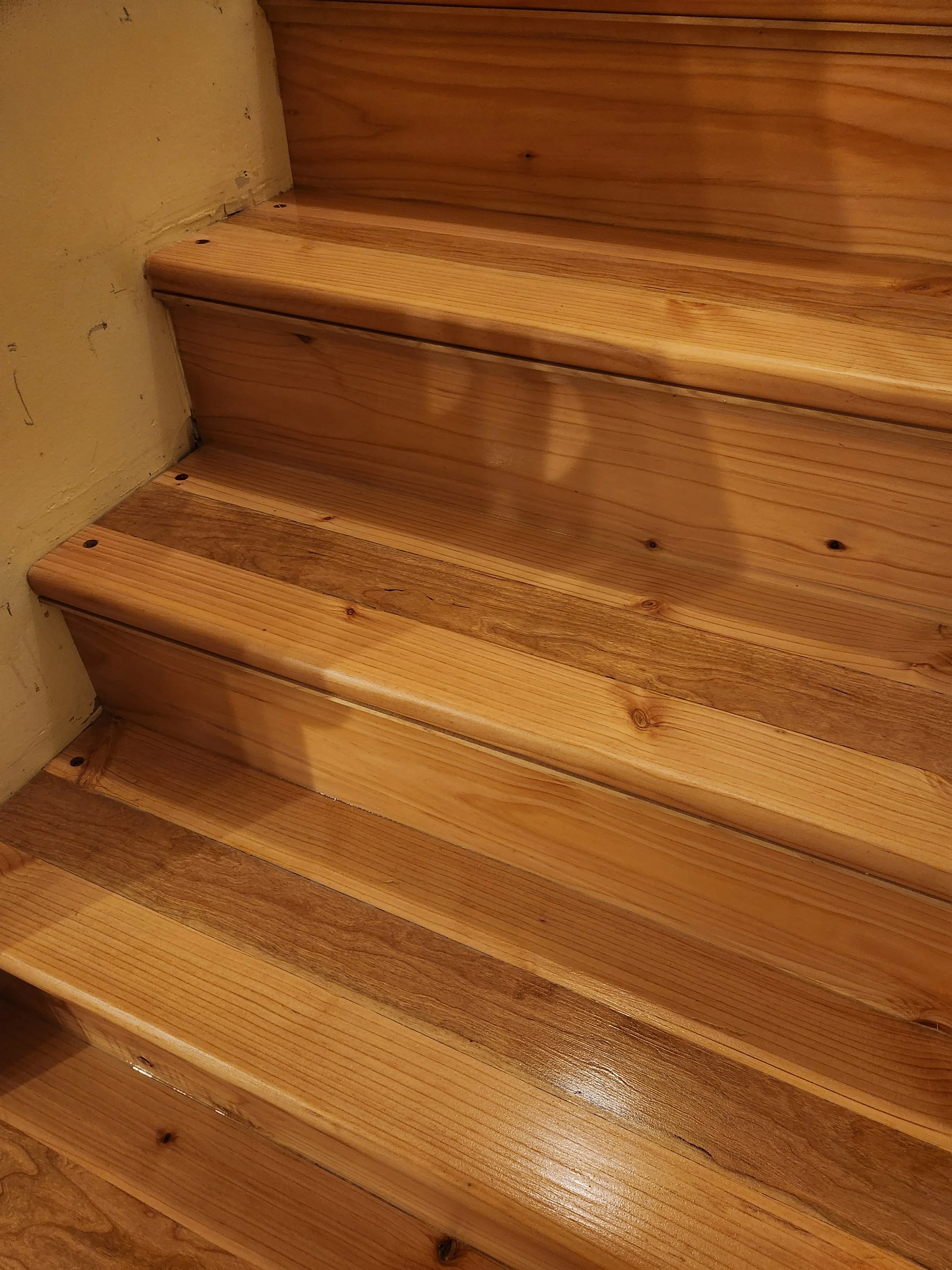Close-up photo of wooden stairs with natural finish, showing the wood grain and knots.