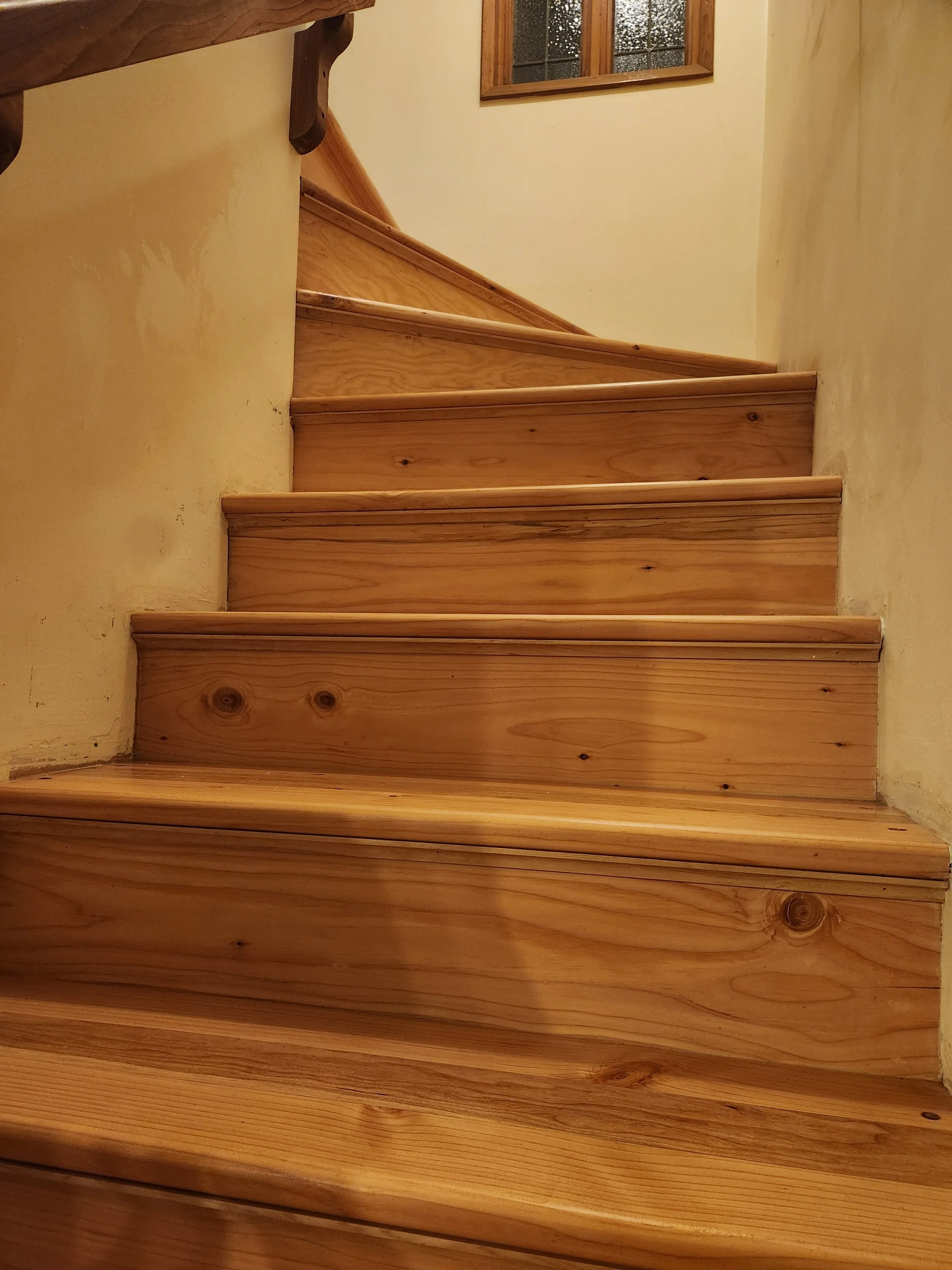 Wooden staircase with a beige wall and a small window above.