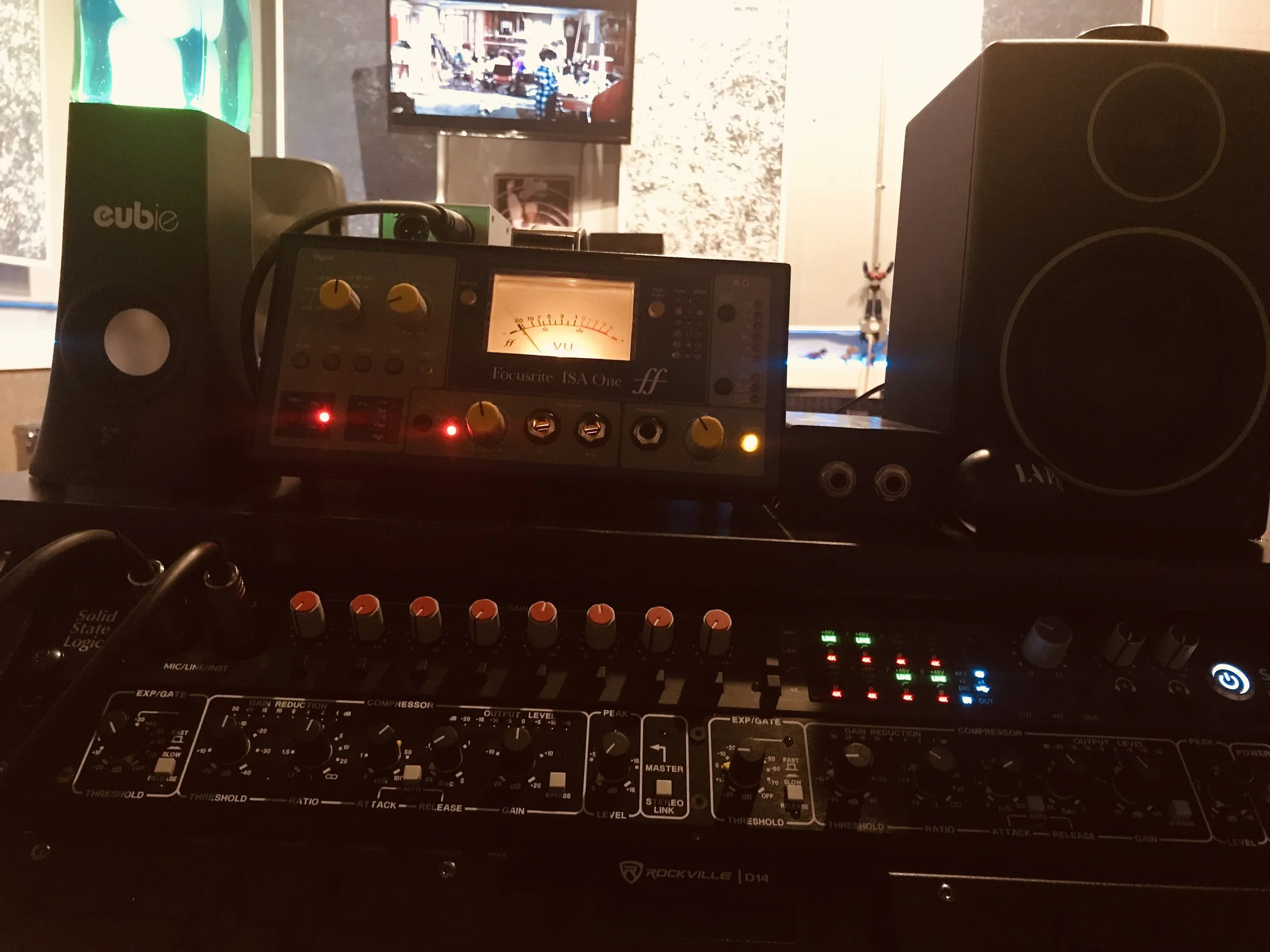 Audio equipment setup including a mixer, speakers, and a monitor speaker, with a television in the background displaying a city street scene.