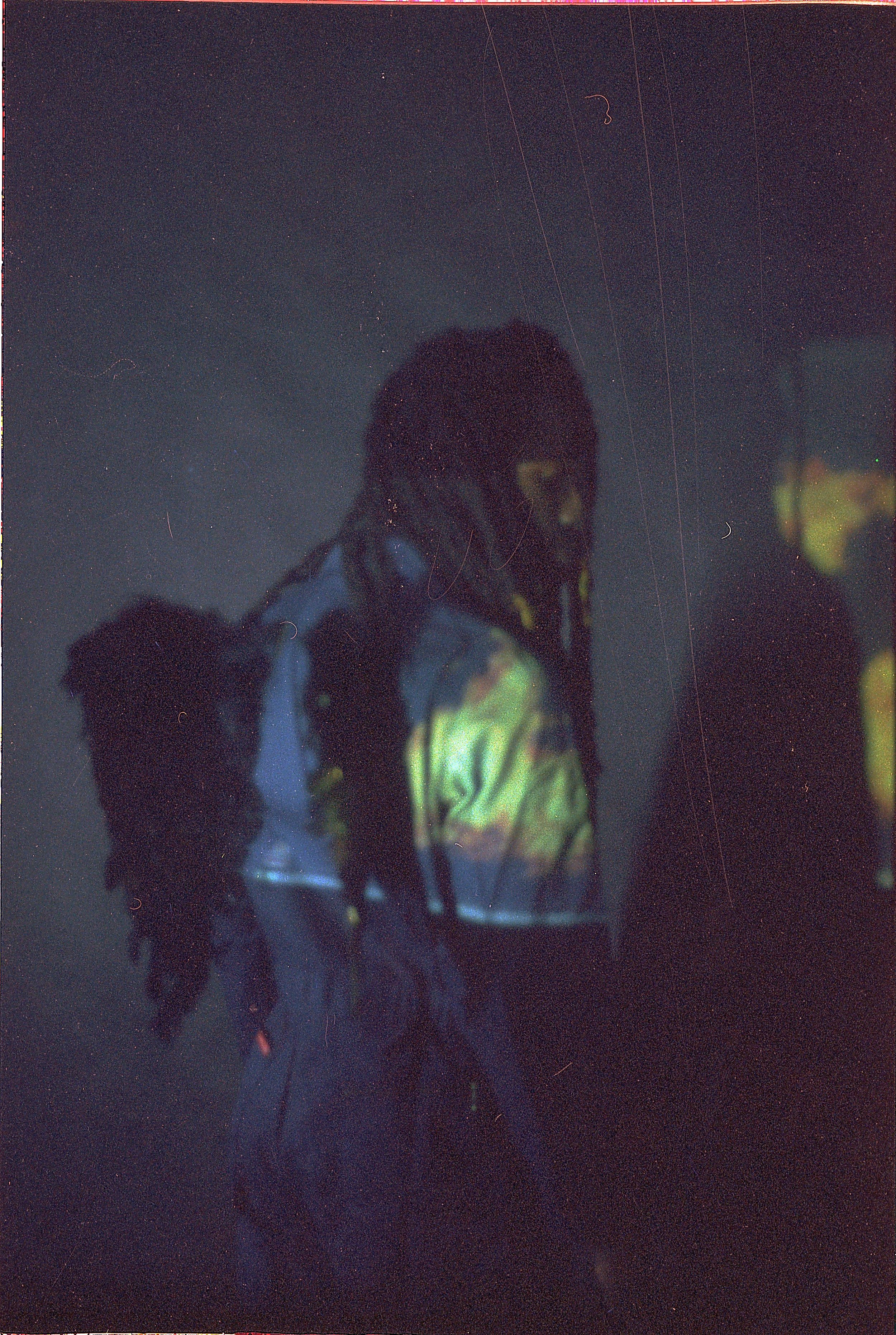 Person with dreadlocks wearing a reflective jacket in a dark setting with faint star-like points of light.
