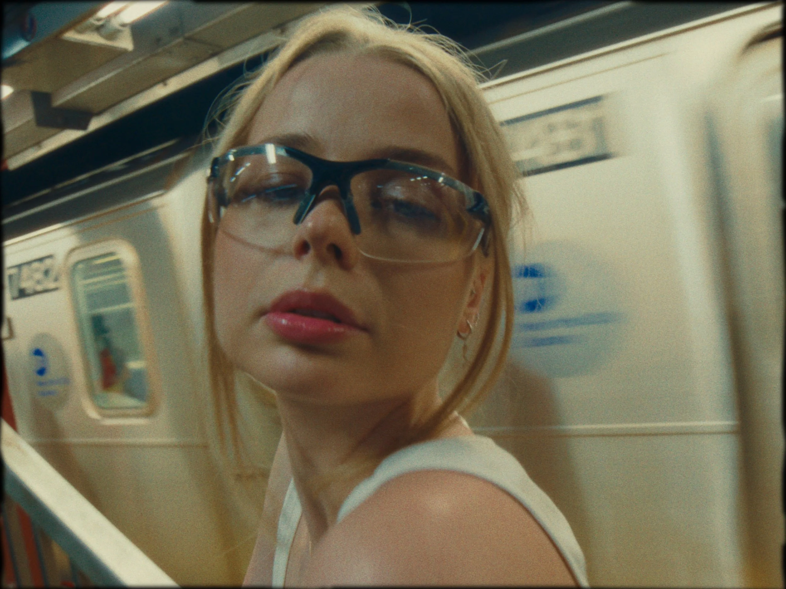 A woman with blonde hair and glasses standing near a subway train in a subway station.