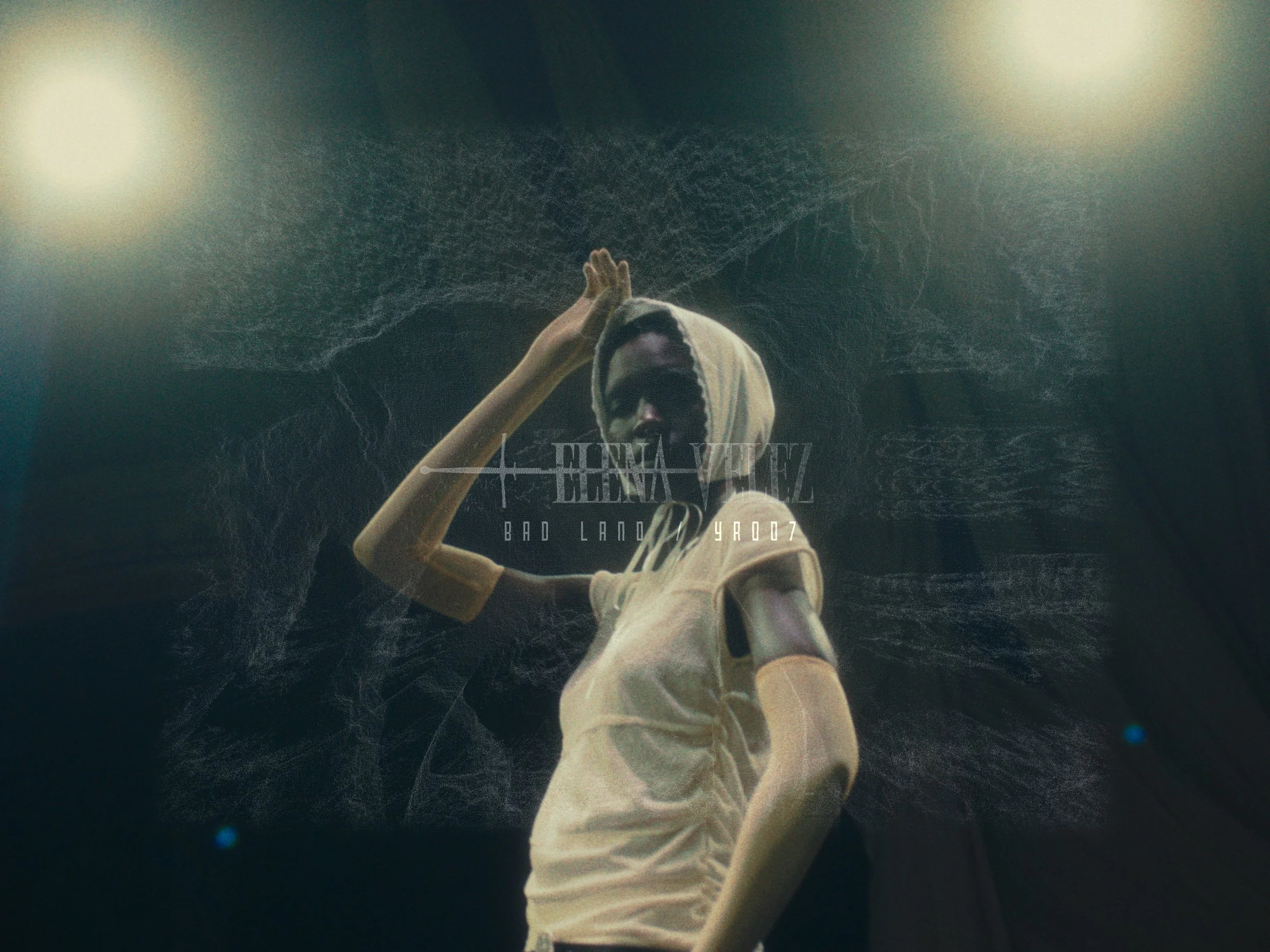 A person wearing a hoodie and a white shirt with a cut-out sleeve, standing in front of a dark background with abstract textures and light flares.