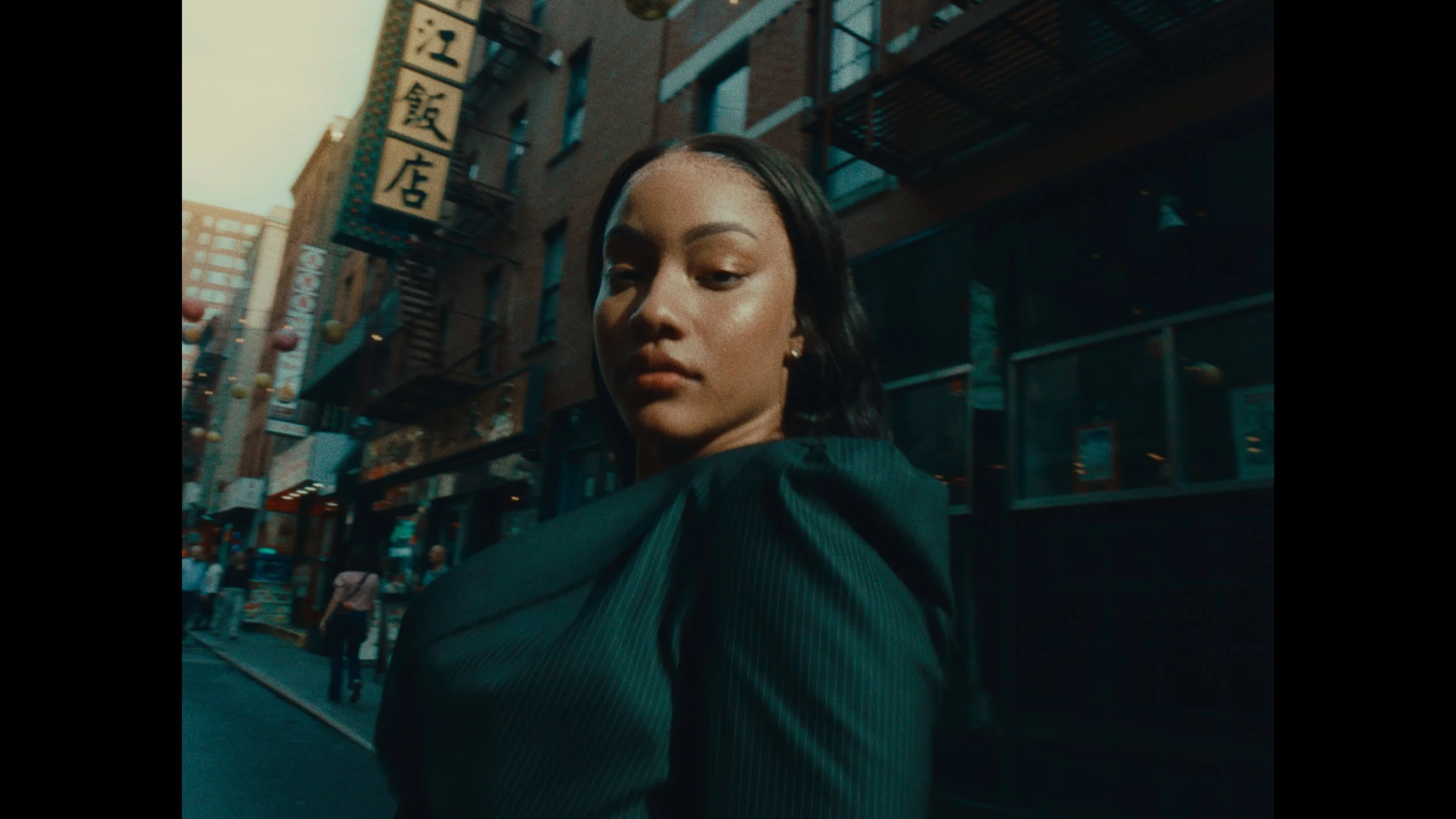 A woman with dark hair and earrings walking in an urban area with Asian signage on buildings.
