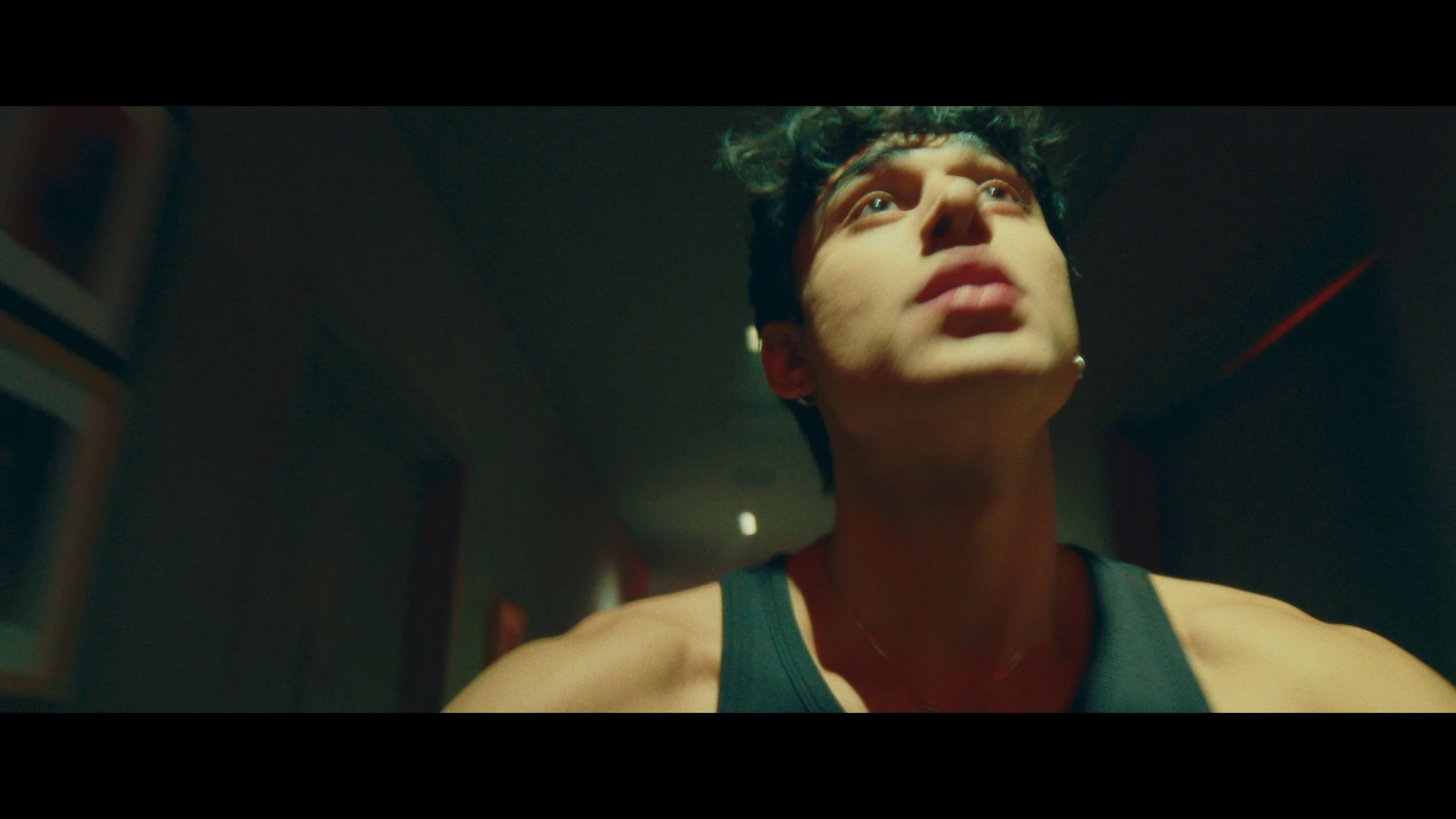Close-up of a young man with curly hair looking upwards in a dimly lit room.