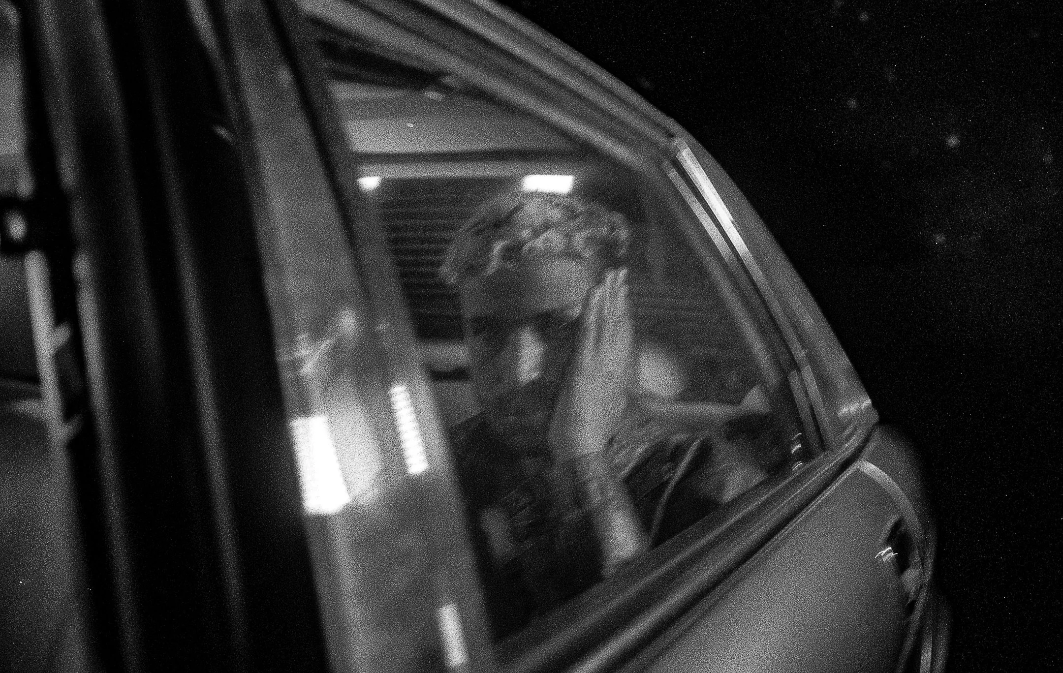 A person inside a spacecraft or space capsule, seen through a window, holding their head with one hand, wearing glasses and a headset, with a dark space background.