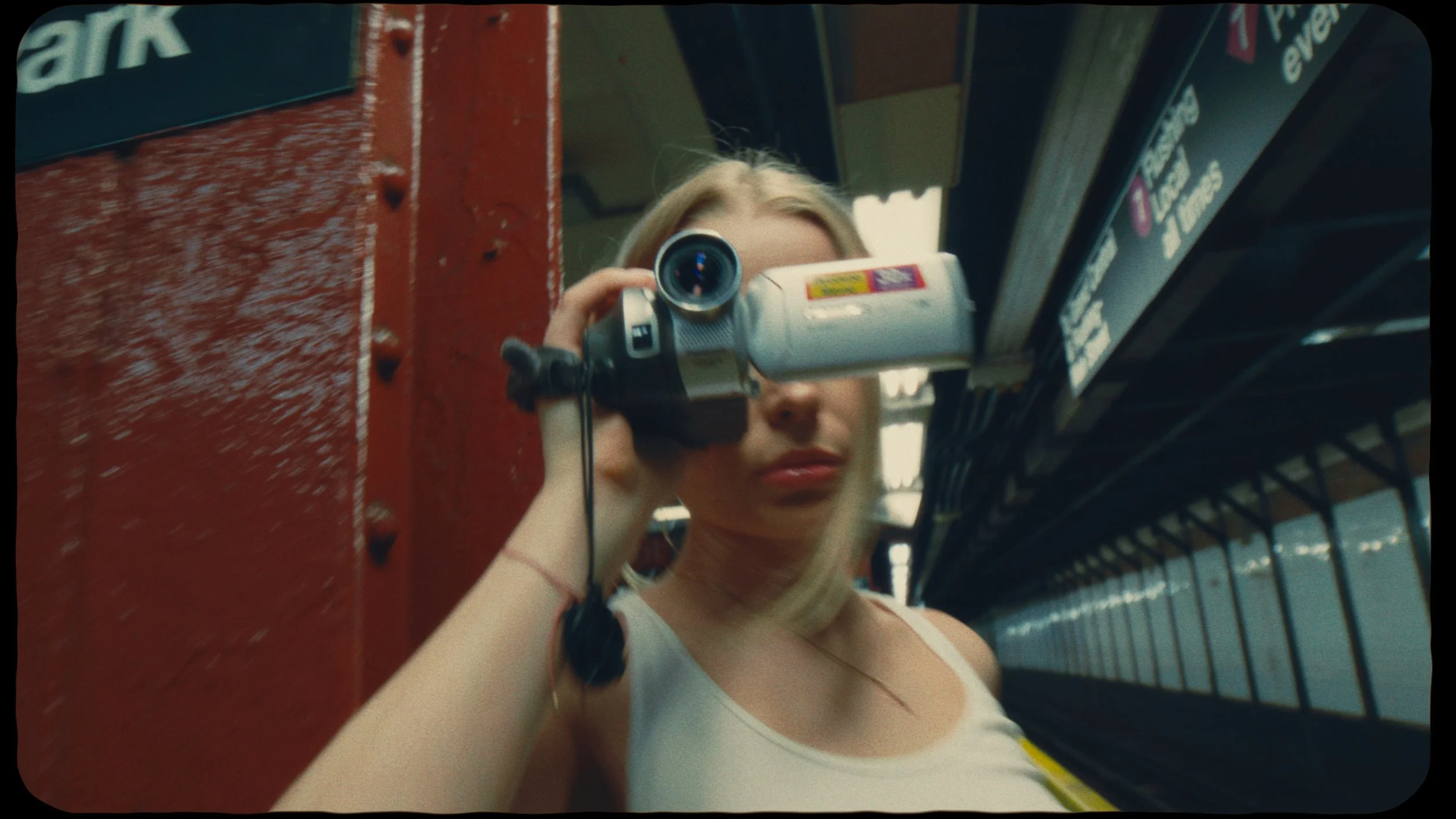 A woman with blonde hair filming with a portable camcorder in a store aisle.