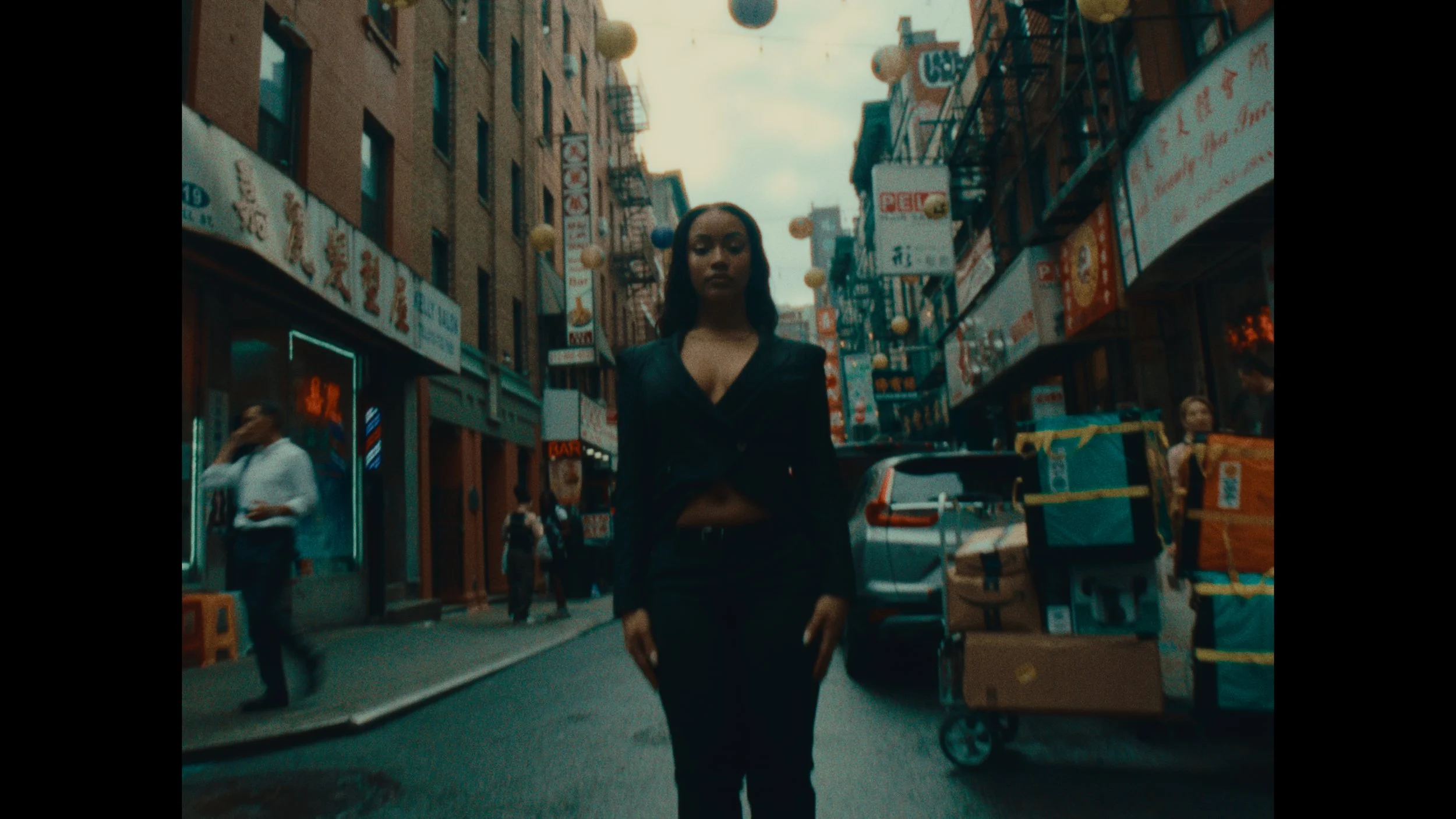 A woman walking on a busy city street in Chinatown, New York City, with shops and signs in Chinese characters in the background.