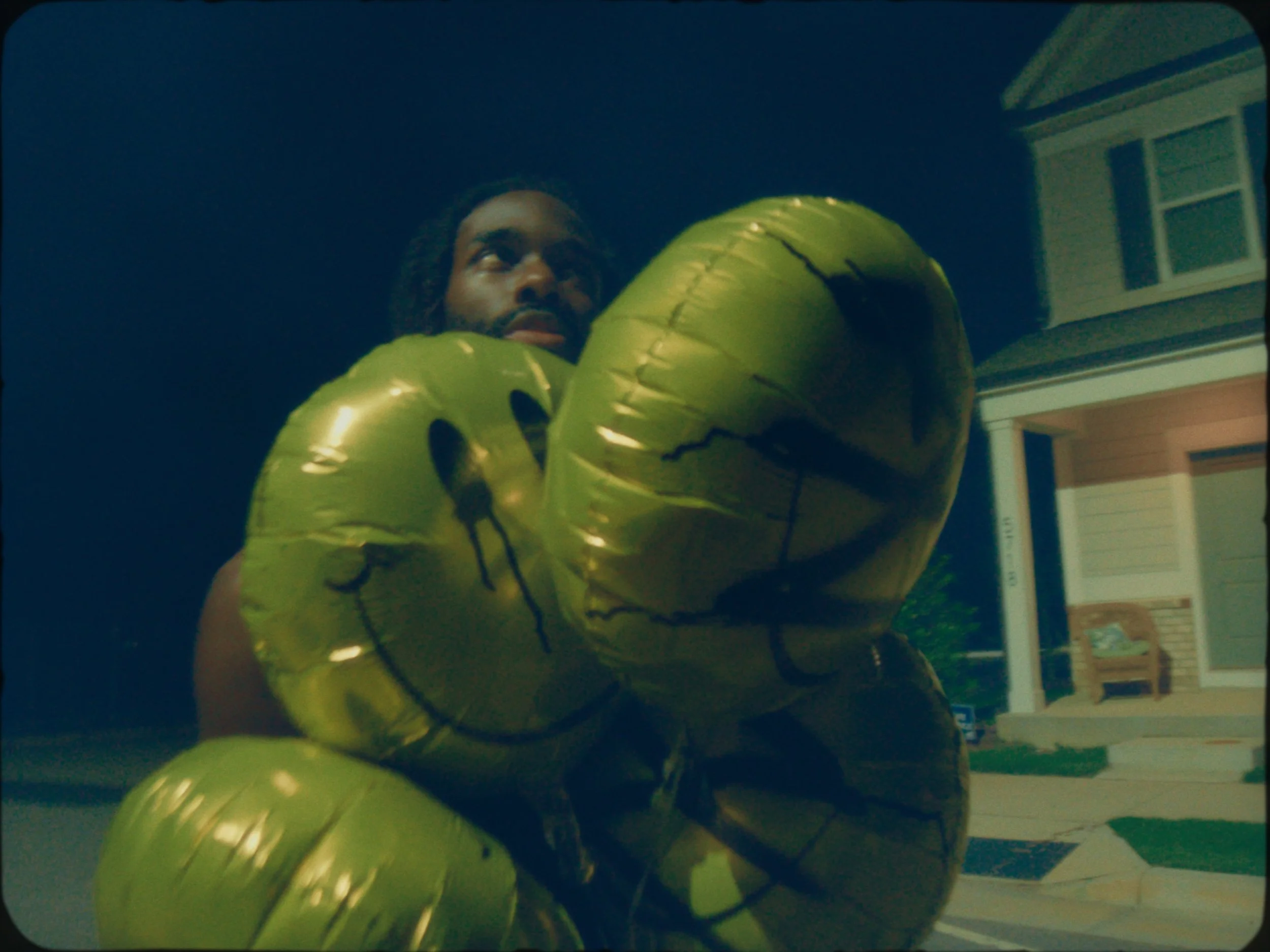 Person holding several yellow smiley face balloons outside at night.
