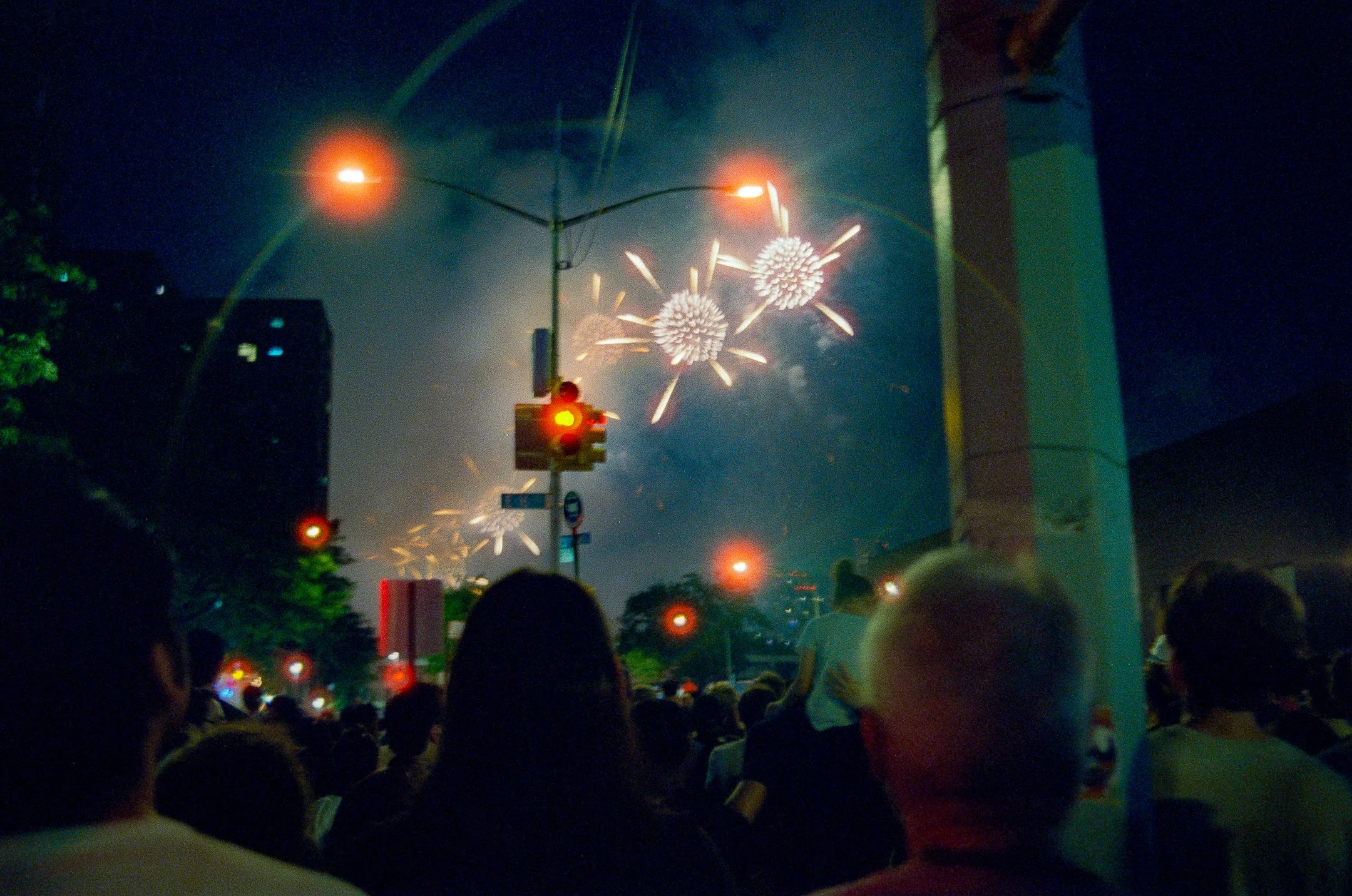 Crowd watching fireworks display at night with fireworks lighting up the sky in the background.