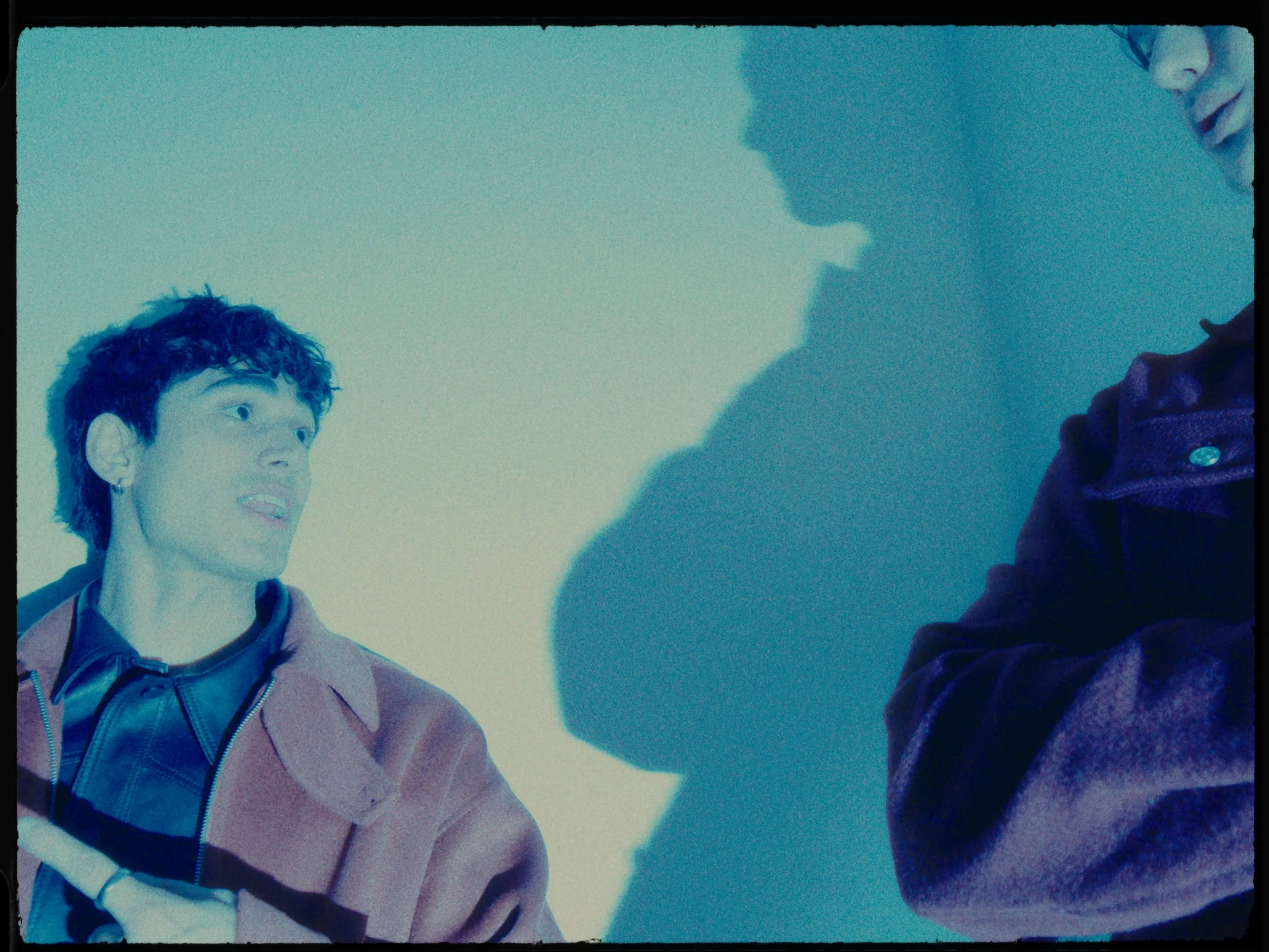 Two people having a conversation, with their shadows cast on the wall. One person is wearing a brown jacket and the other is wearing a dark jacket.