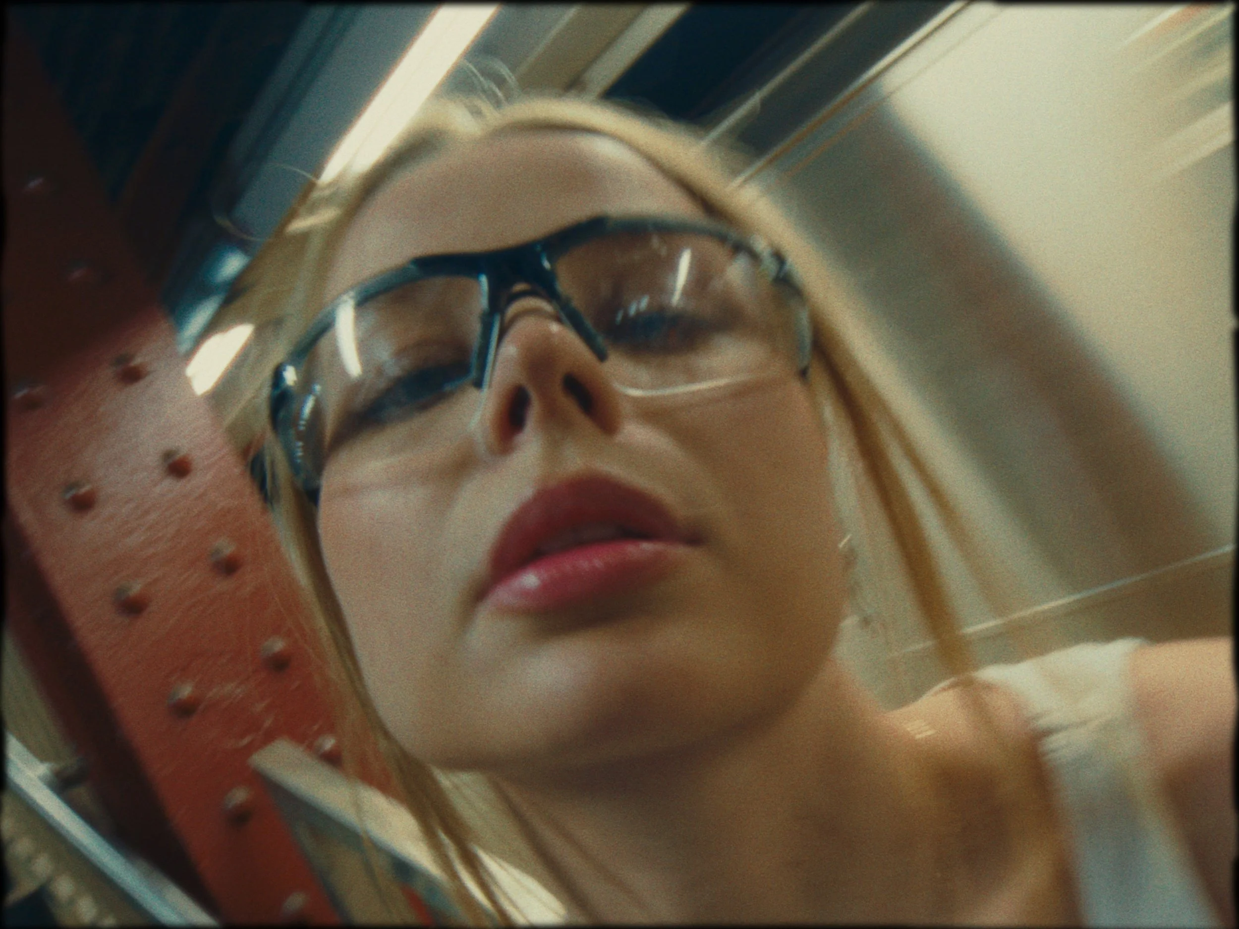 Close-up of a woman wearing glasses looking downward, with her face reflected in a mirror.
