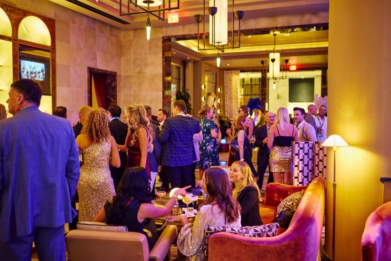 People mingling at a lively indoor party or event in a stylish venue with warm lighting and modern decor.