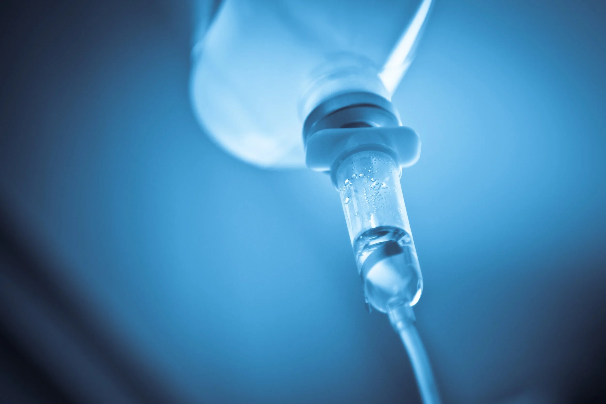 Close-up of a hanging IV bag filled with clear liquid connected to a tube and IV port.