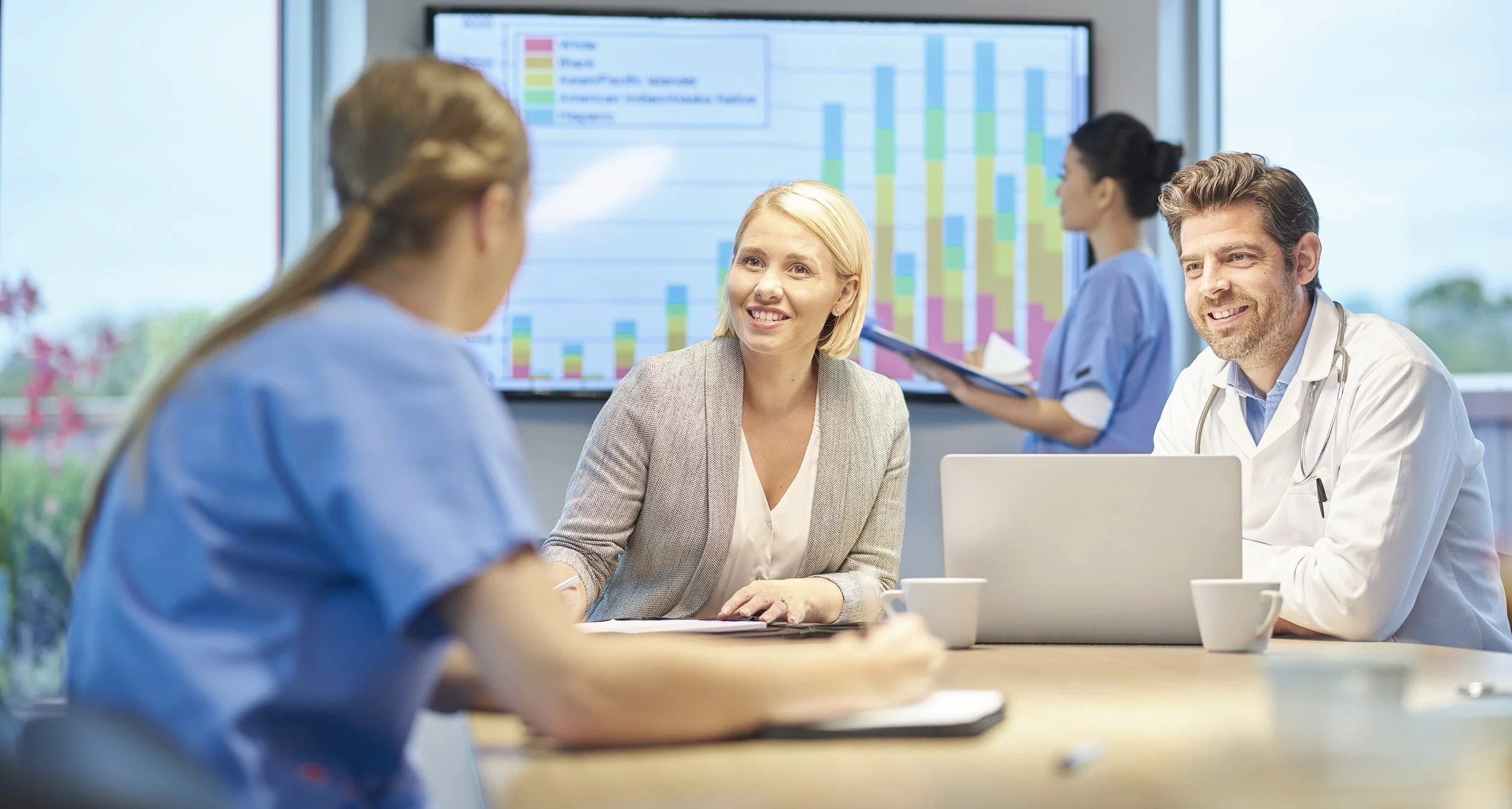 Medical professionals having a discussion in a conference room with a large screen displaying charts and data.