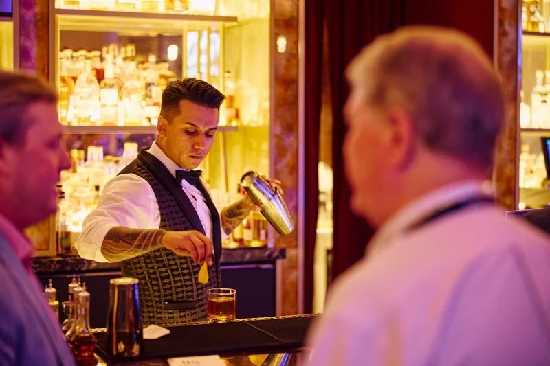 Bartender pouring a drink at a bar with a neon-lit glass shelf behind him