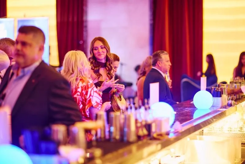People socializing at a bar or reception with colorful lighting and modern decor.