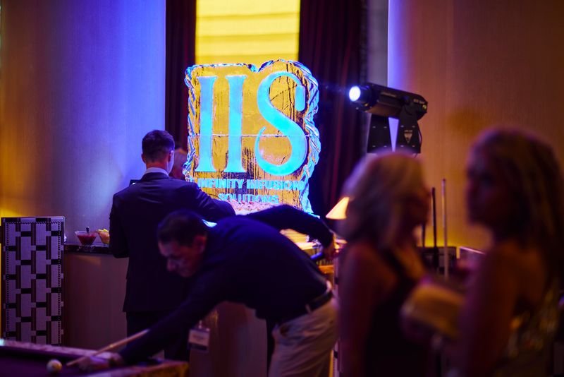 People playing pool at a social event with a large illuminated sign reading 'IIS' in the background.