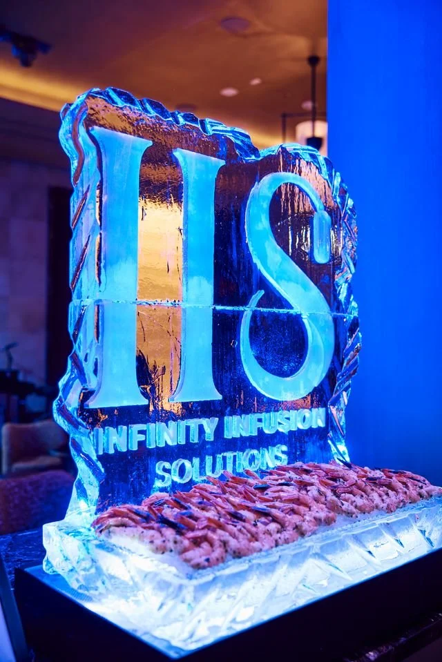 An ice sculpture with the logo 'UIS' and the words 'Ininity Infusion Solutions' engraved on it, with a bed of shrimp at the base.