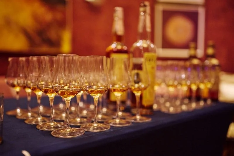 A row of empty wine glasses and bottles on a table in a dimly lit setting.