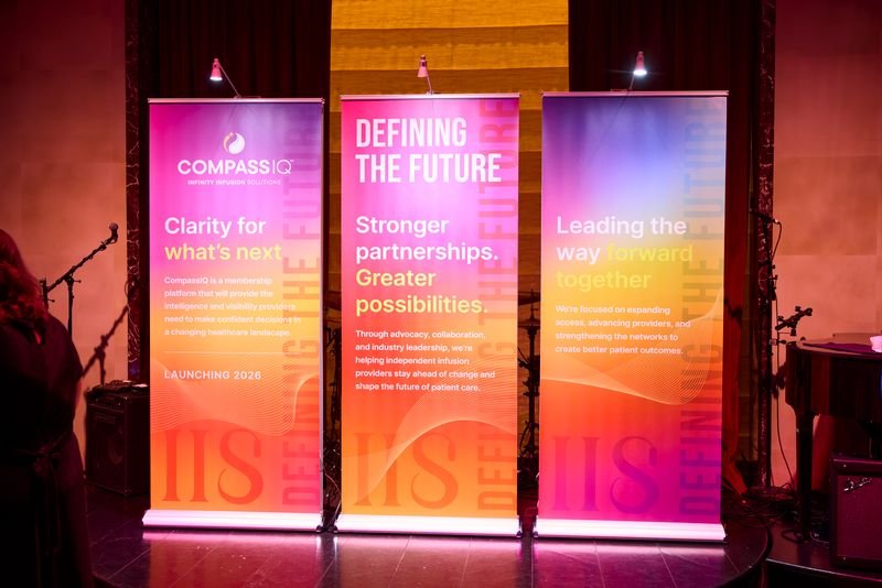 Three vertical banners on a stage with microphones and music equipment. The banners feature the COMPASS IQ logo and text about future partnerships, industry leadership, and innovation.