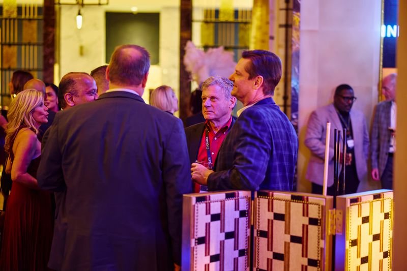 People socializing at a formal event or party in a well-lit venue with bookshelves and modern decor.