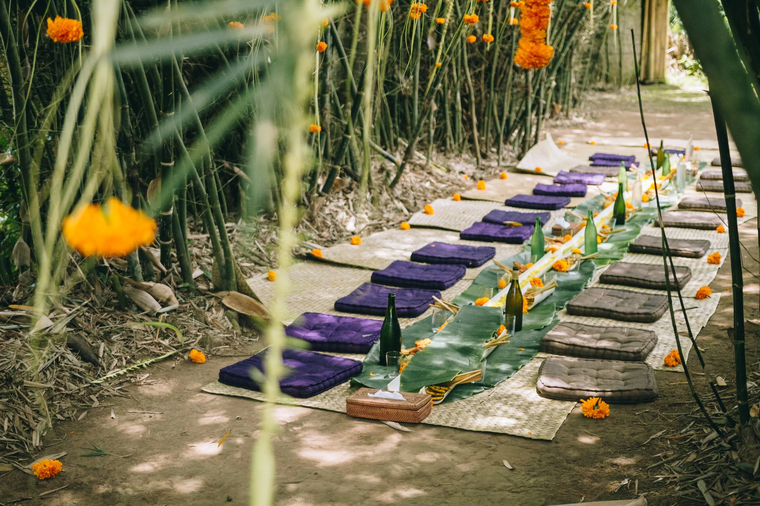 Yoga mats, cushions, and bottles arranged on mats in an outdoor setting with flowers and foliage.