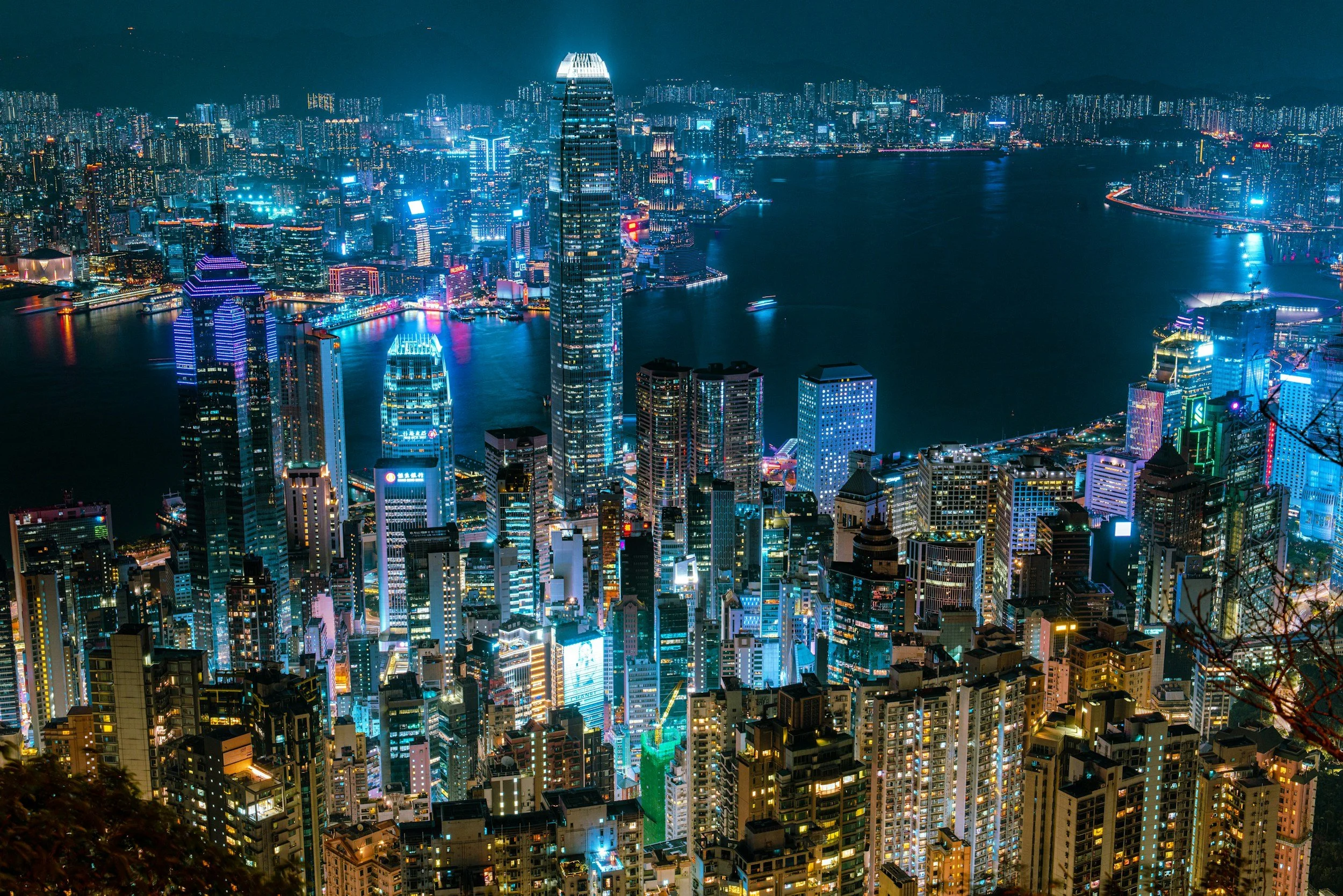 Nighttime cityscape of Hong Kong with illuminated skyscrapers, harbor, and brightly lit buildings.