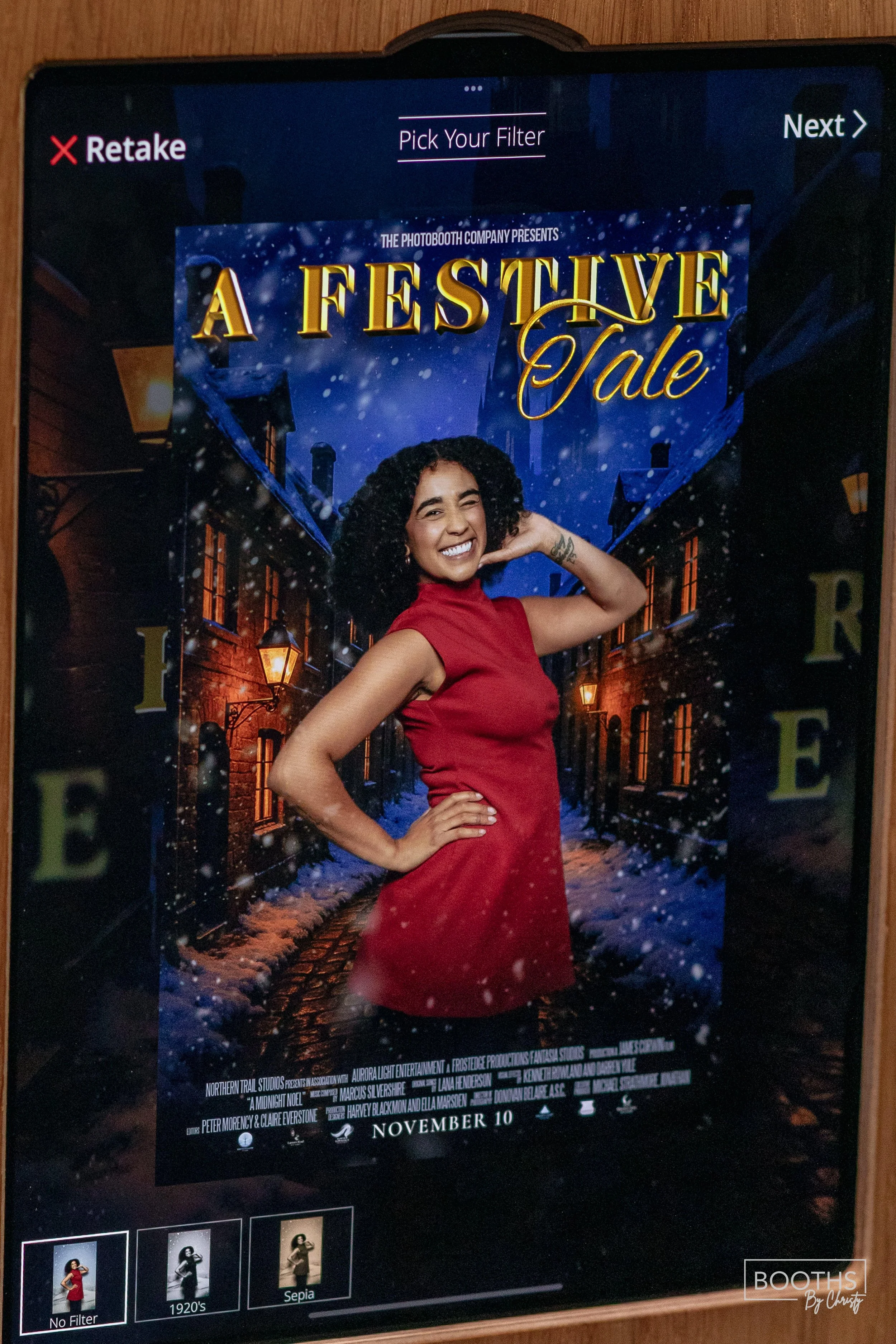 A promotional poster for a holiday-themed photo booth titled 'A Festive Tale,' showing a woman in a red dress smiling at the camera with a snowy street scene in the background.