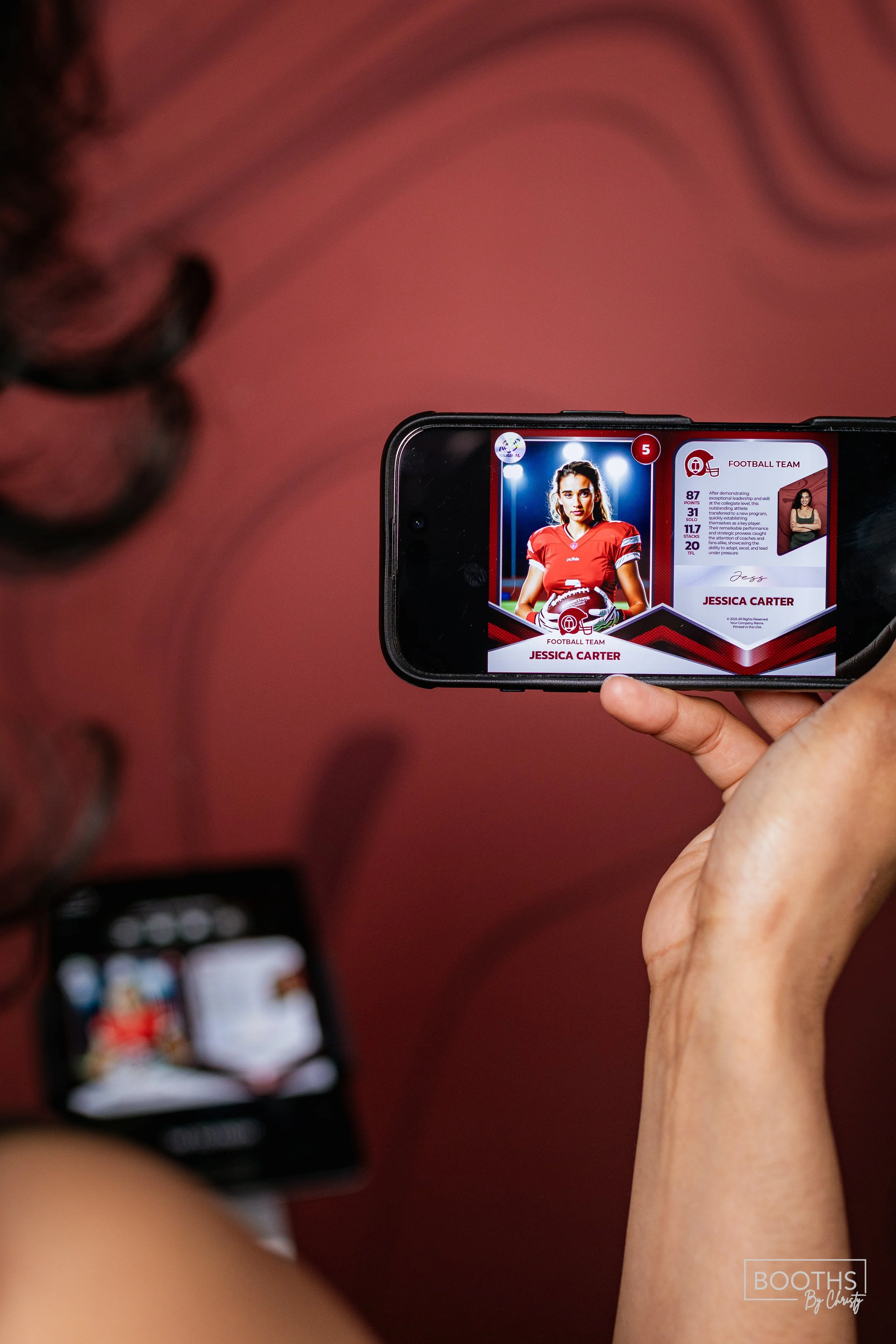 A person taking a photo of a sports trading card of Jessica Carter in a football jersey on their smartphone, with a blurred wristwatch visible on their arm against a pink background.