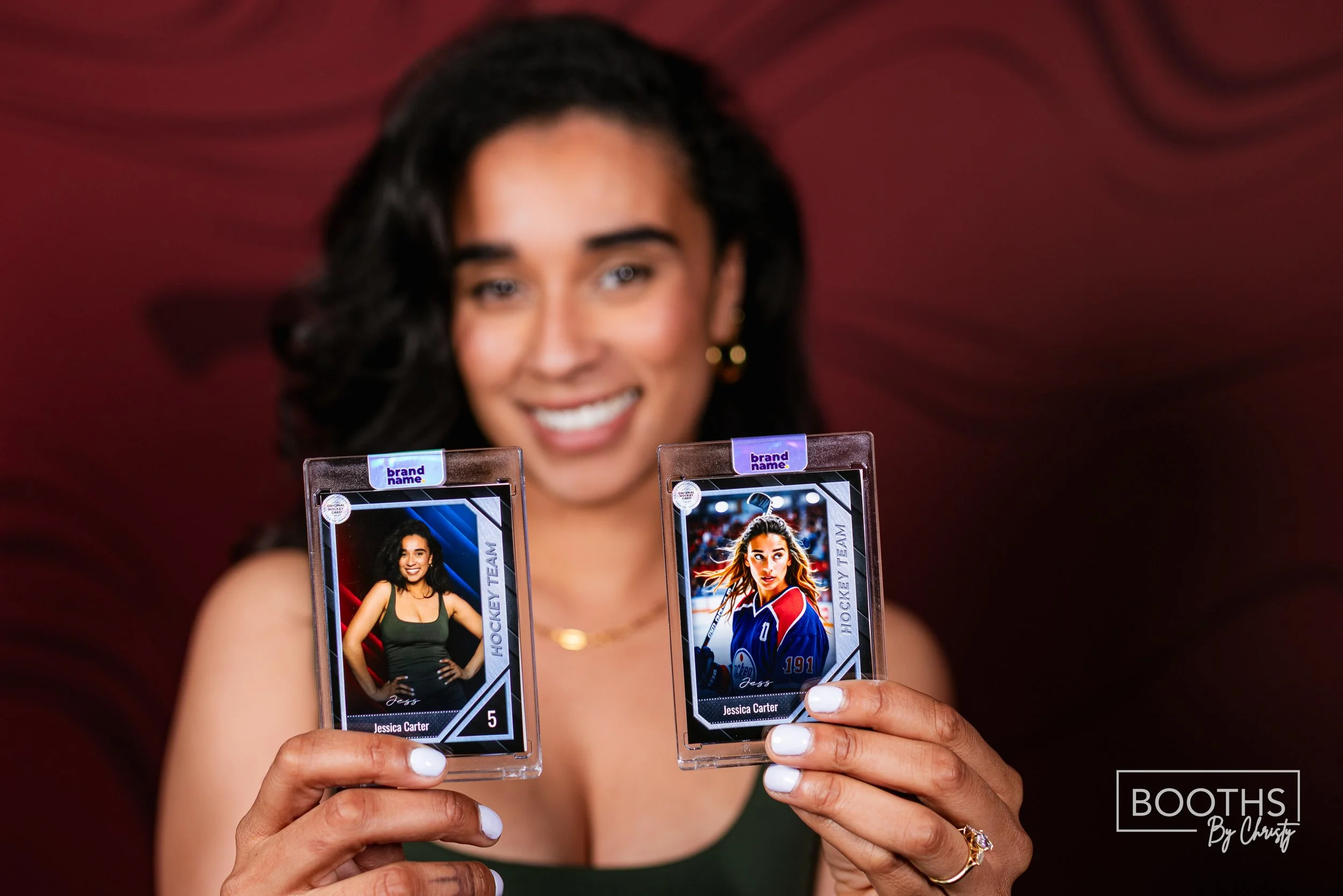 Woman holding two hockey trading cards smiling at camera with a blurred maroon background.
