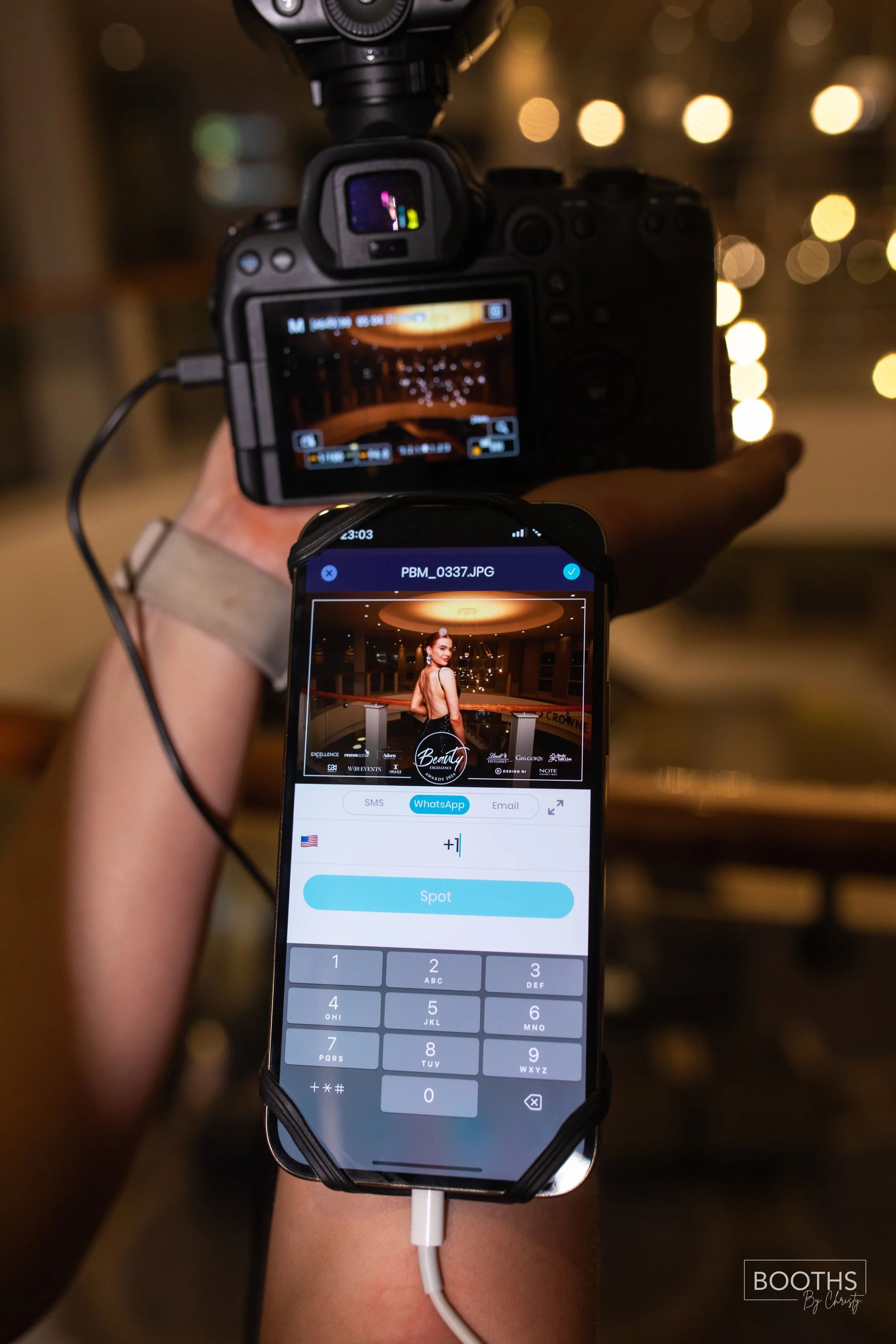 A camera is being used to take a photograph of a woman in an indoor setting, with a smartphone displaying the image of the woman being taken.