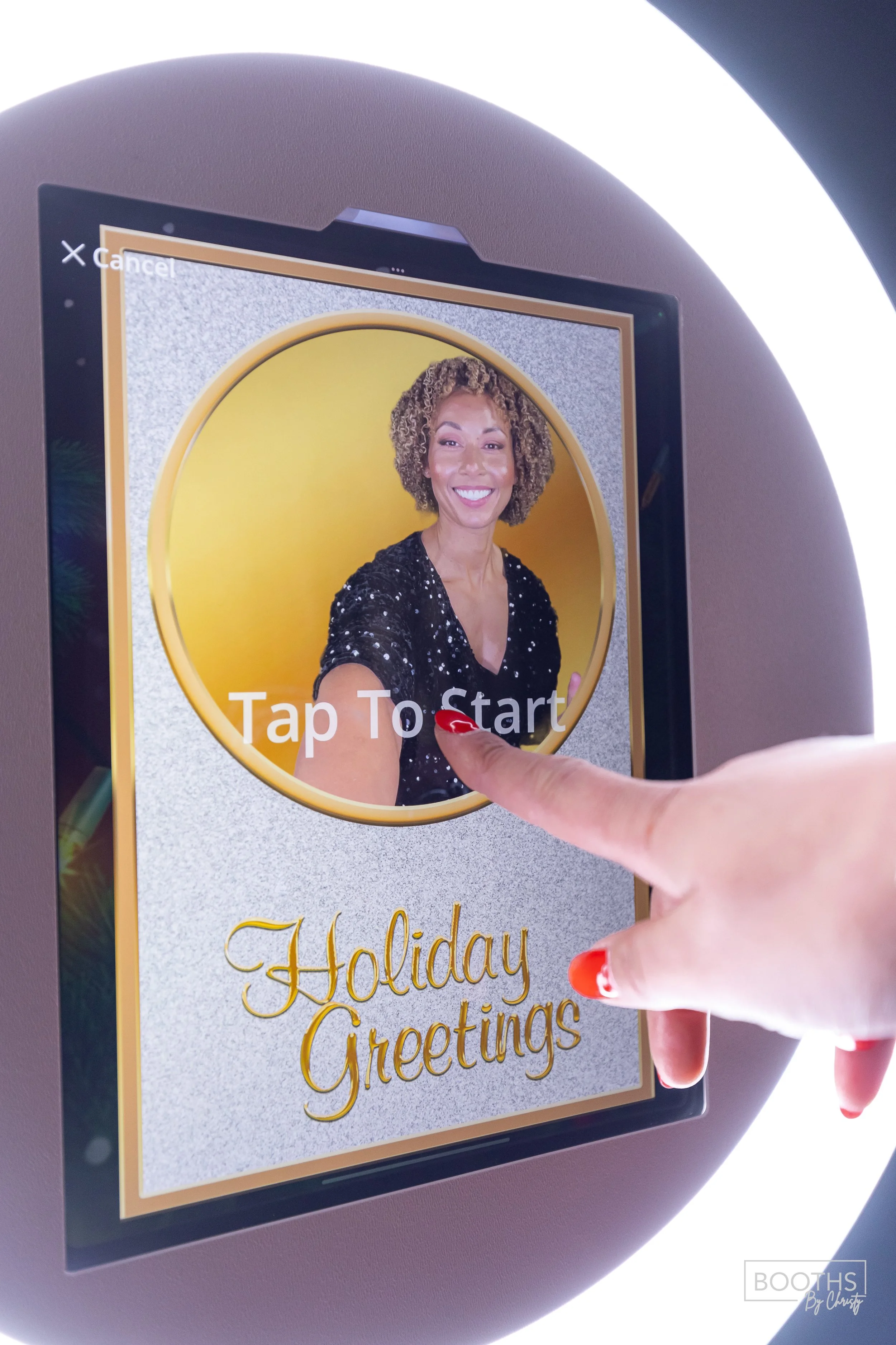 A person with red nail polish touches a screen displaying a smiling woman with curly hair against a yellow background. The screen has the text "Tap To Start" and