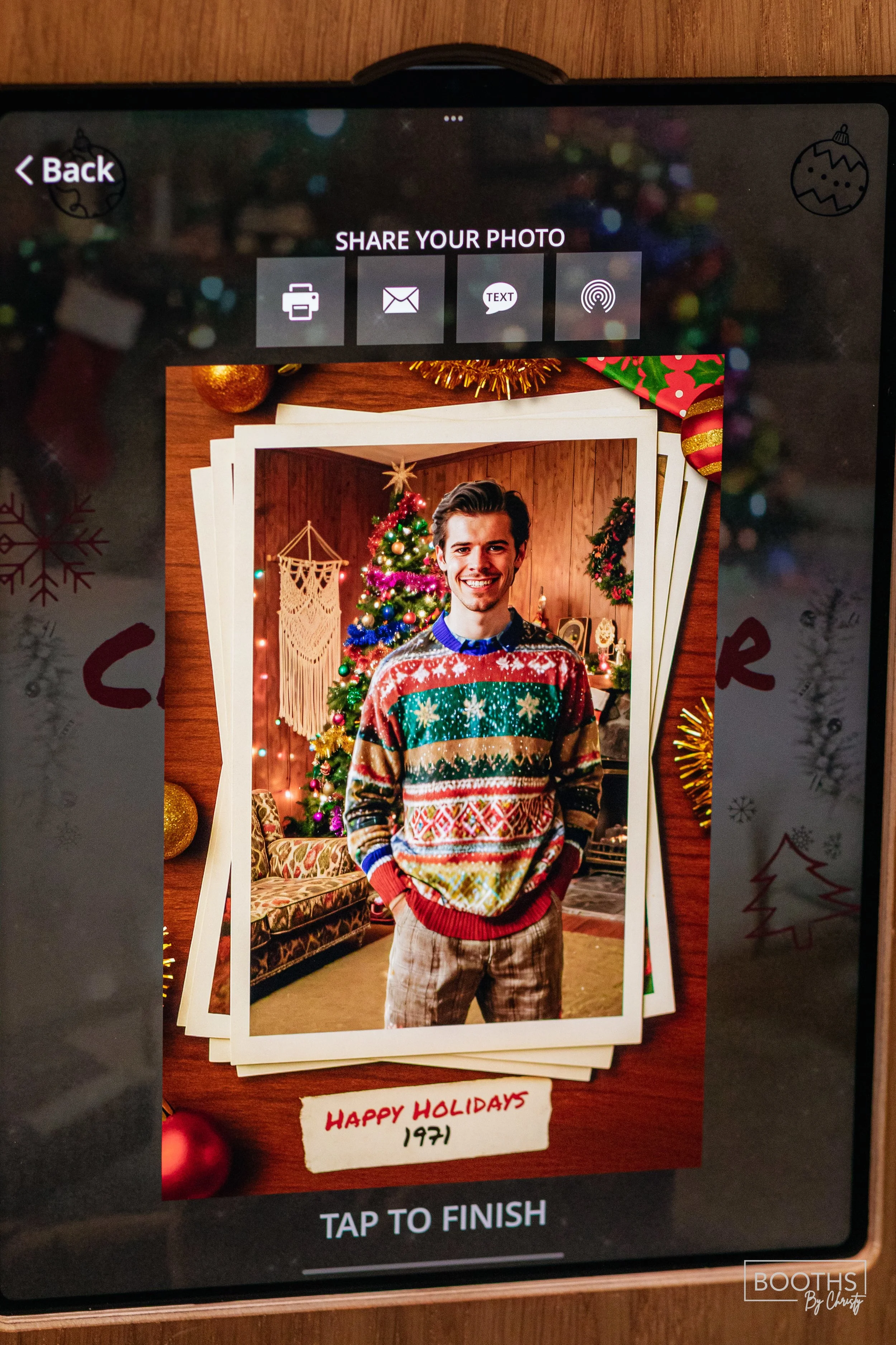 Photograph of a young man in a holiday sweater standing in a decorated room with a Christmas tree, ornaments, and festive decorations.
