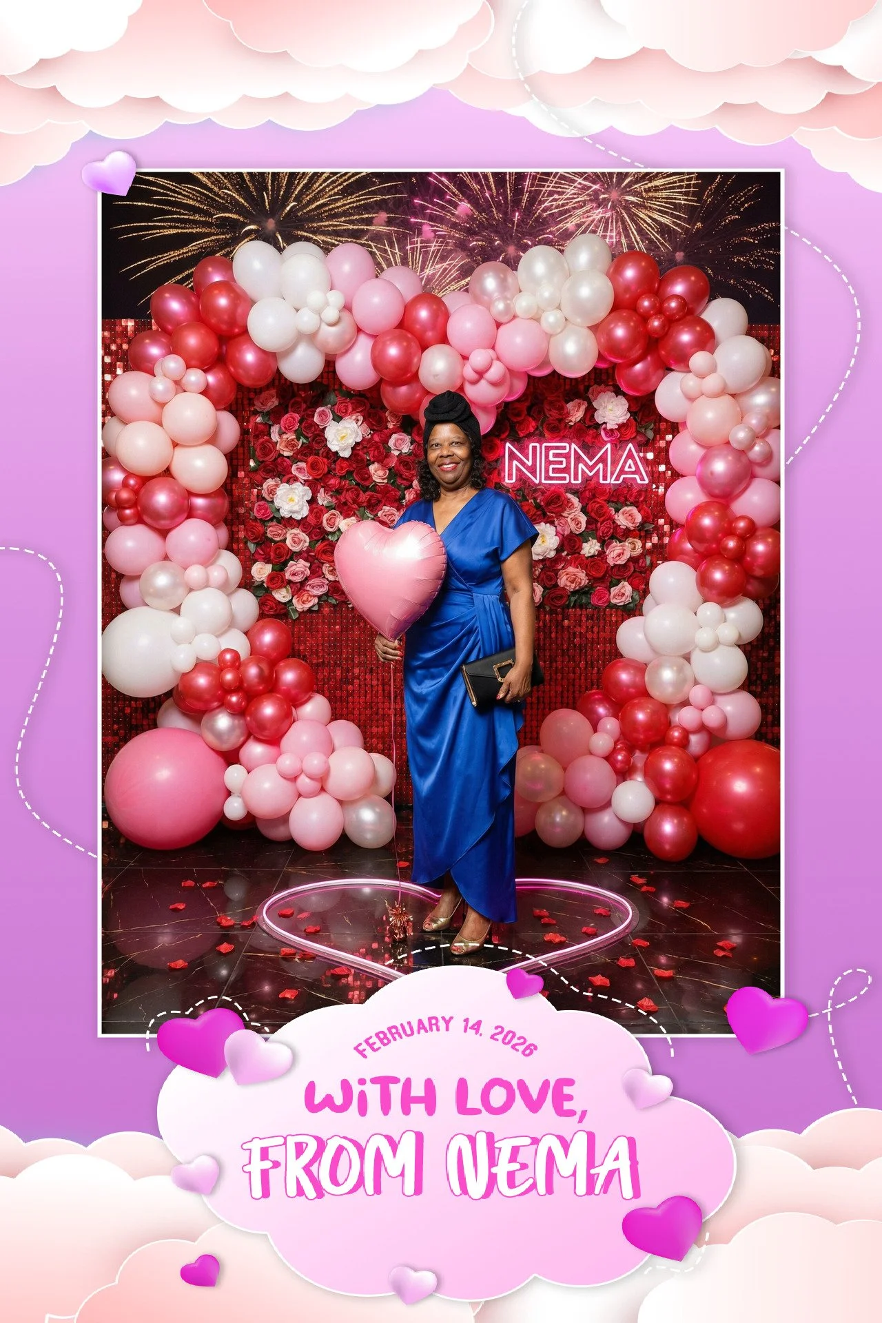 Woman in a blue dress holding a pink heart-shaped balloon, standing in front of a heart-shaped balloon and flower arch with a backdrop of fireworks, with a sign that reads 'NEMA'.