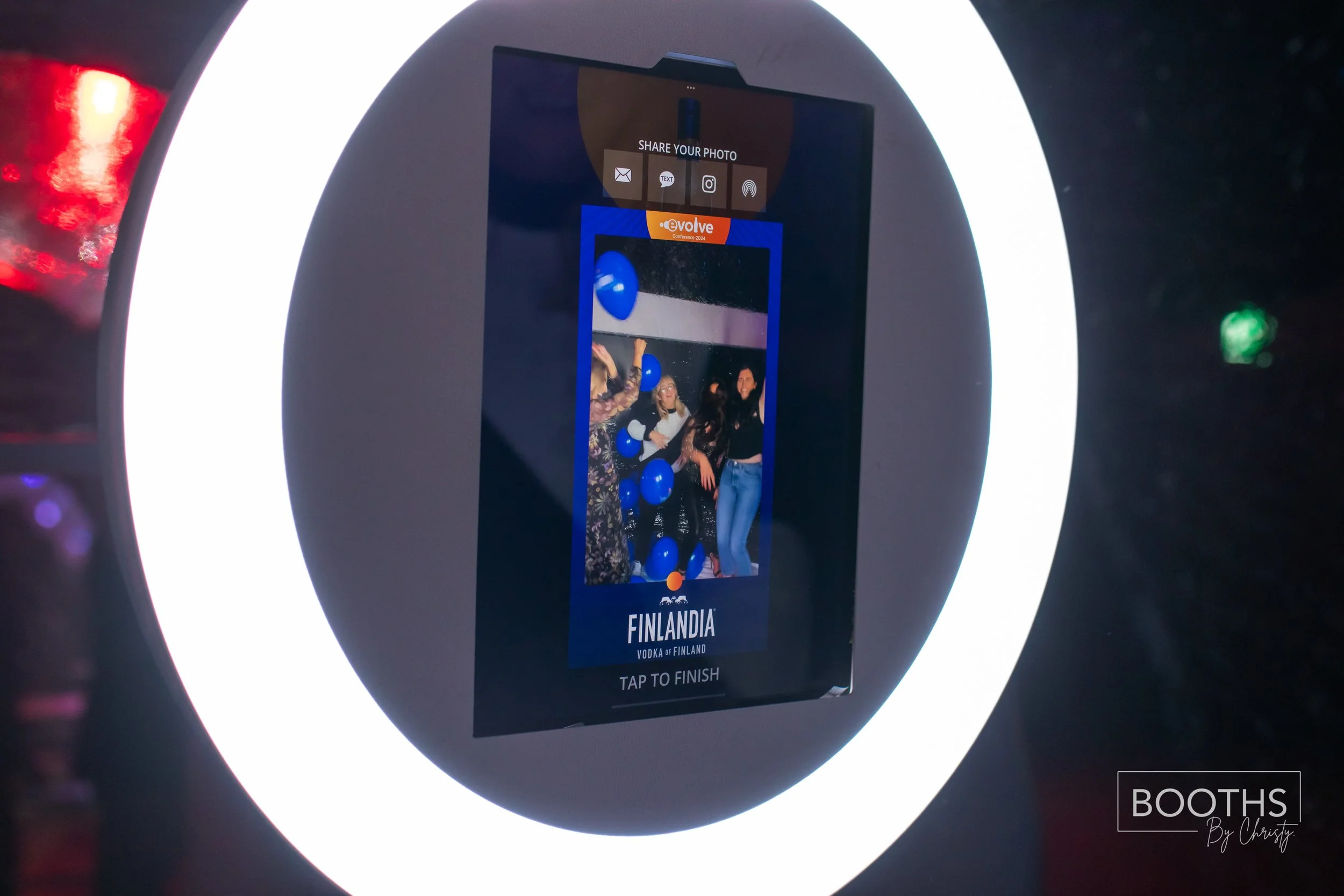 Photo booth with a ring light, showing a screen capturing a group of people at a party with blue balloons, labeled Finlandia vodka.
