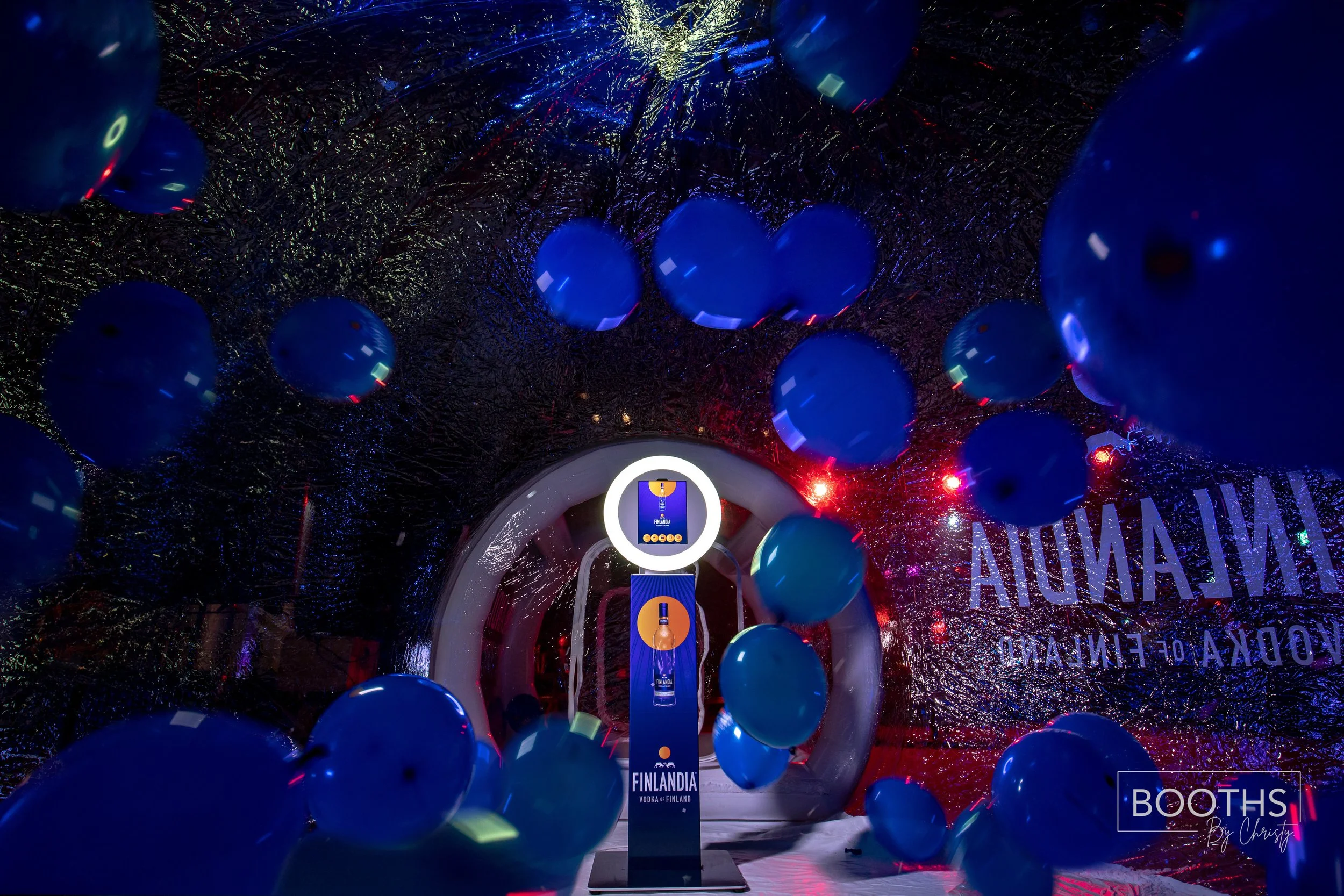 Display window decorated with blue balloons and holographic streamers, featuring a vodka brand sign for Finlandia, with a circular lighted frame and promotional stand inside.