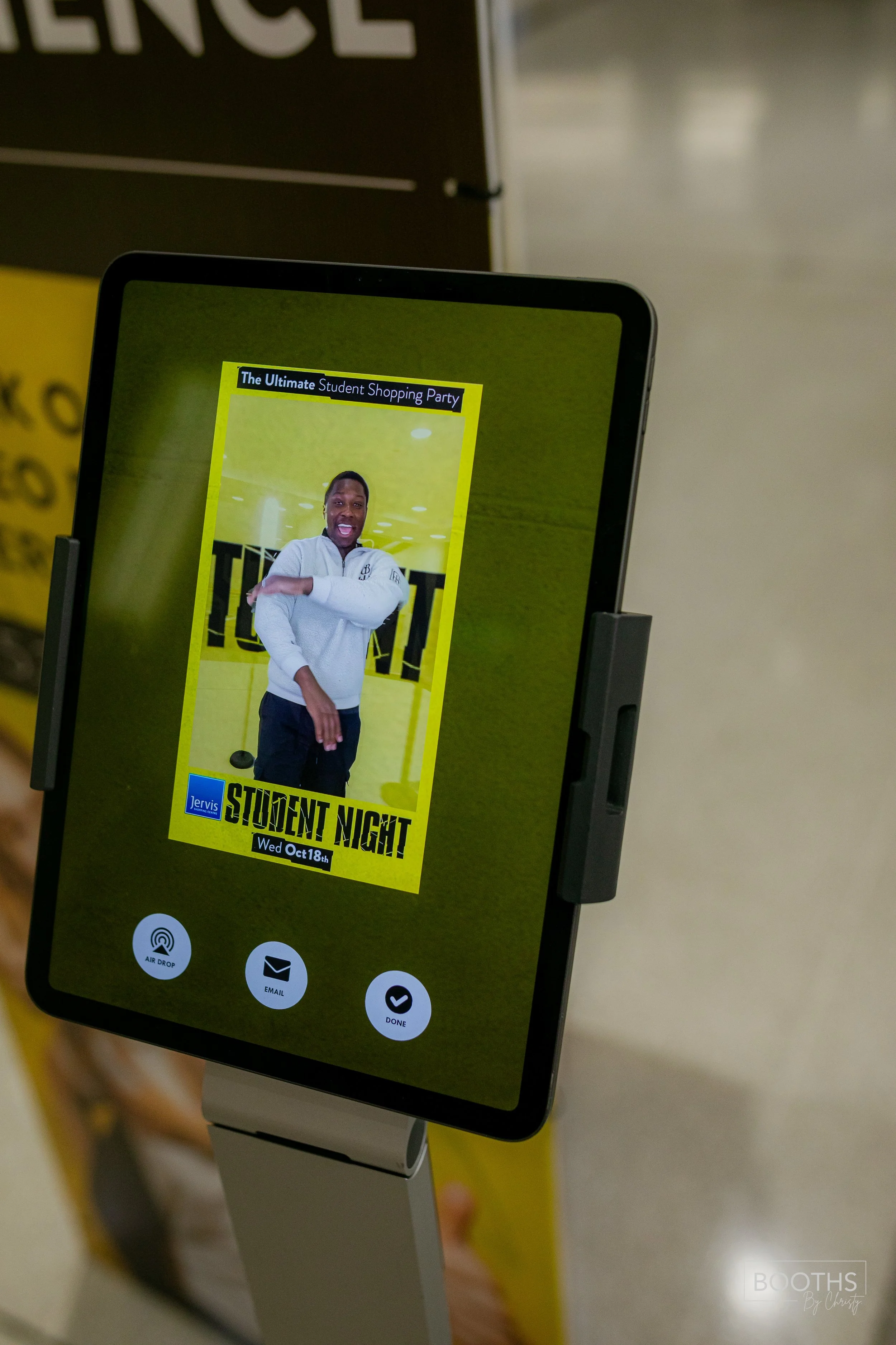 A digital display screen advertising a student shopping event, showing a smiling person stretching their arm, with details about 'Student Night' on October 18th.